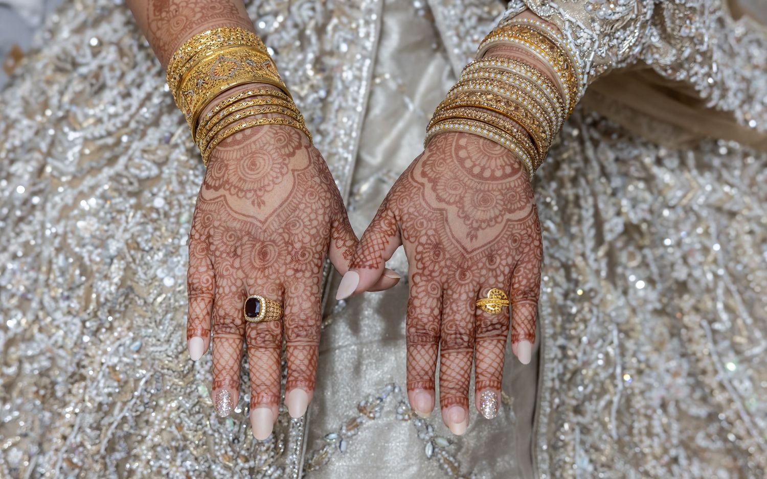 Close-up of bride's hands with detailed henna mehndi patterns, gold bangles, and rings on wedding day.