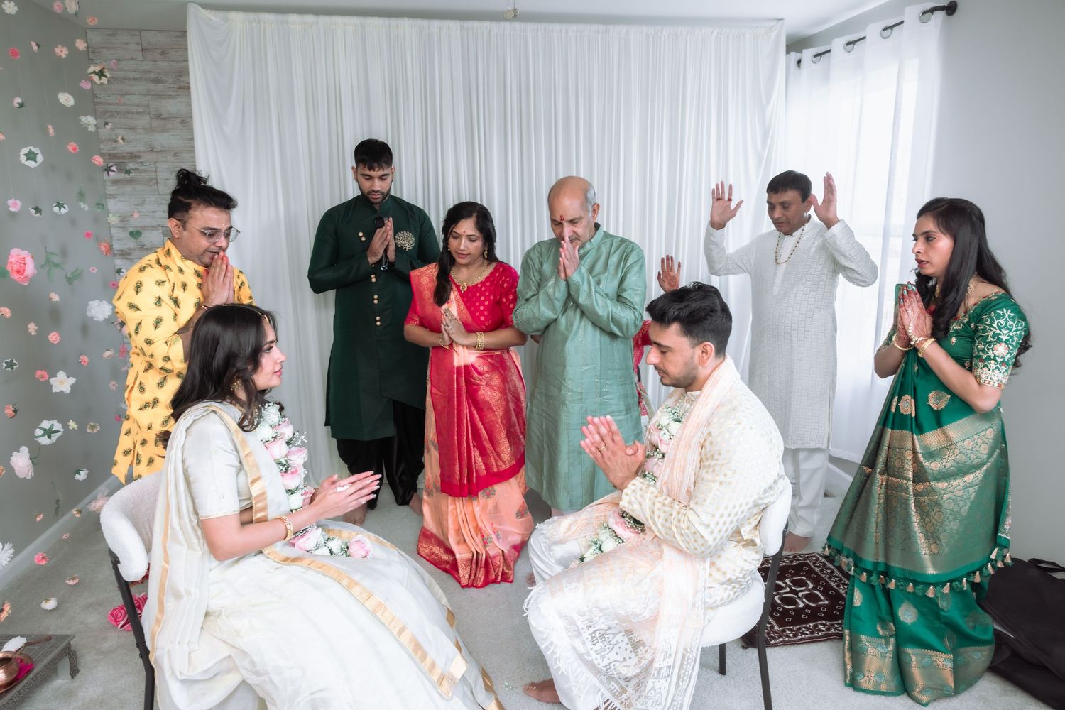 Family and guests perform Namaste gesture blessing the couple during a traditional Indian wedding ceremony.