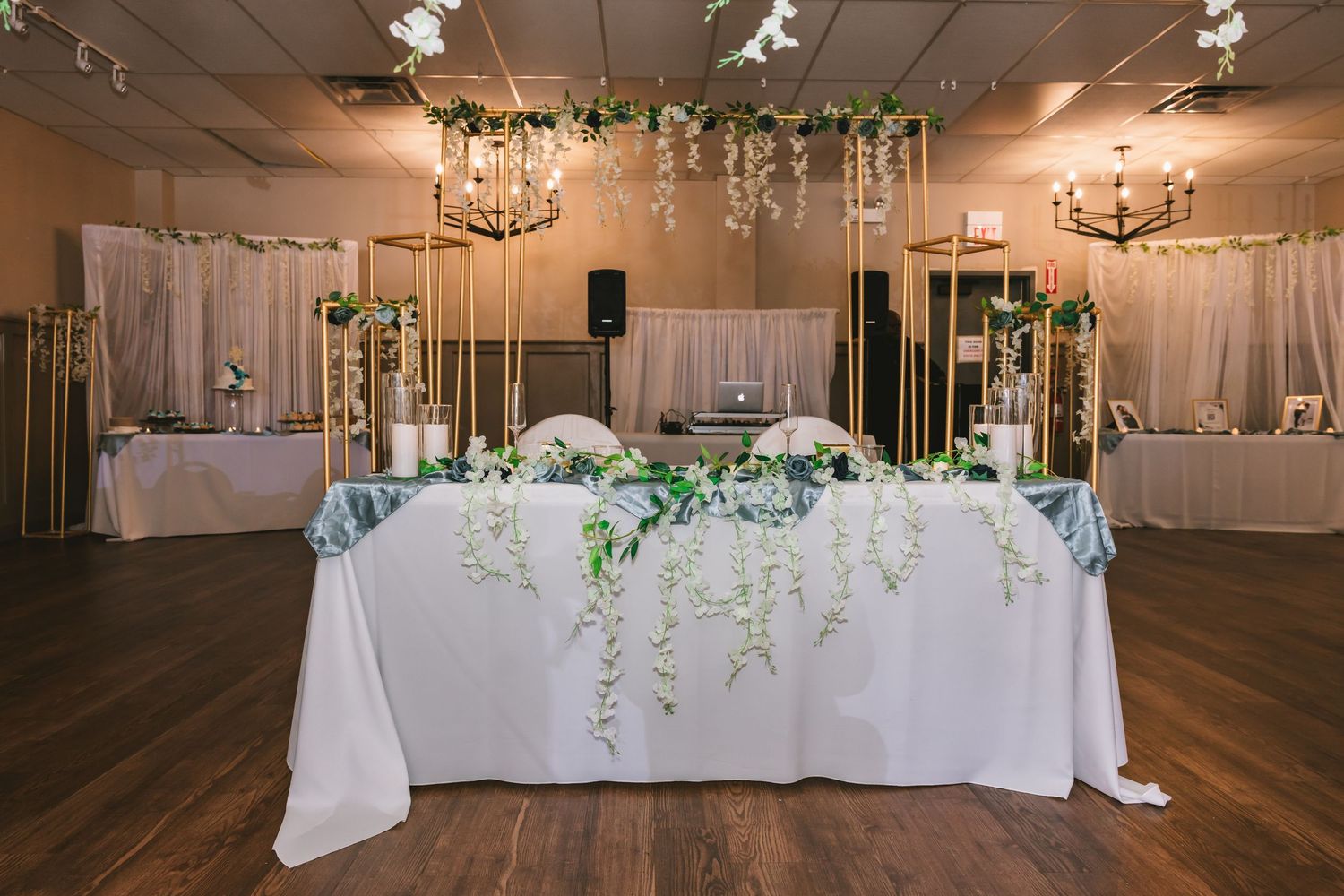 Wedding reception sweetheart table with white linens, cascading greenery, and gold floral arch decorations.