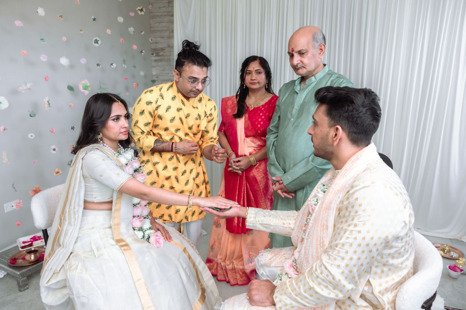 Family members gather as bride in white lehenga participates in a traditional South Asian wedding ritual ceremony.