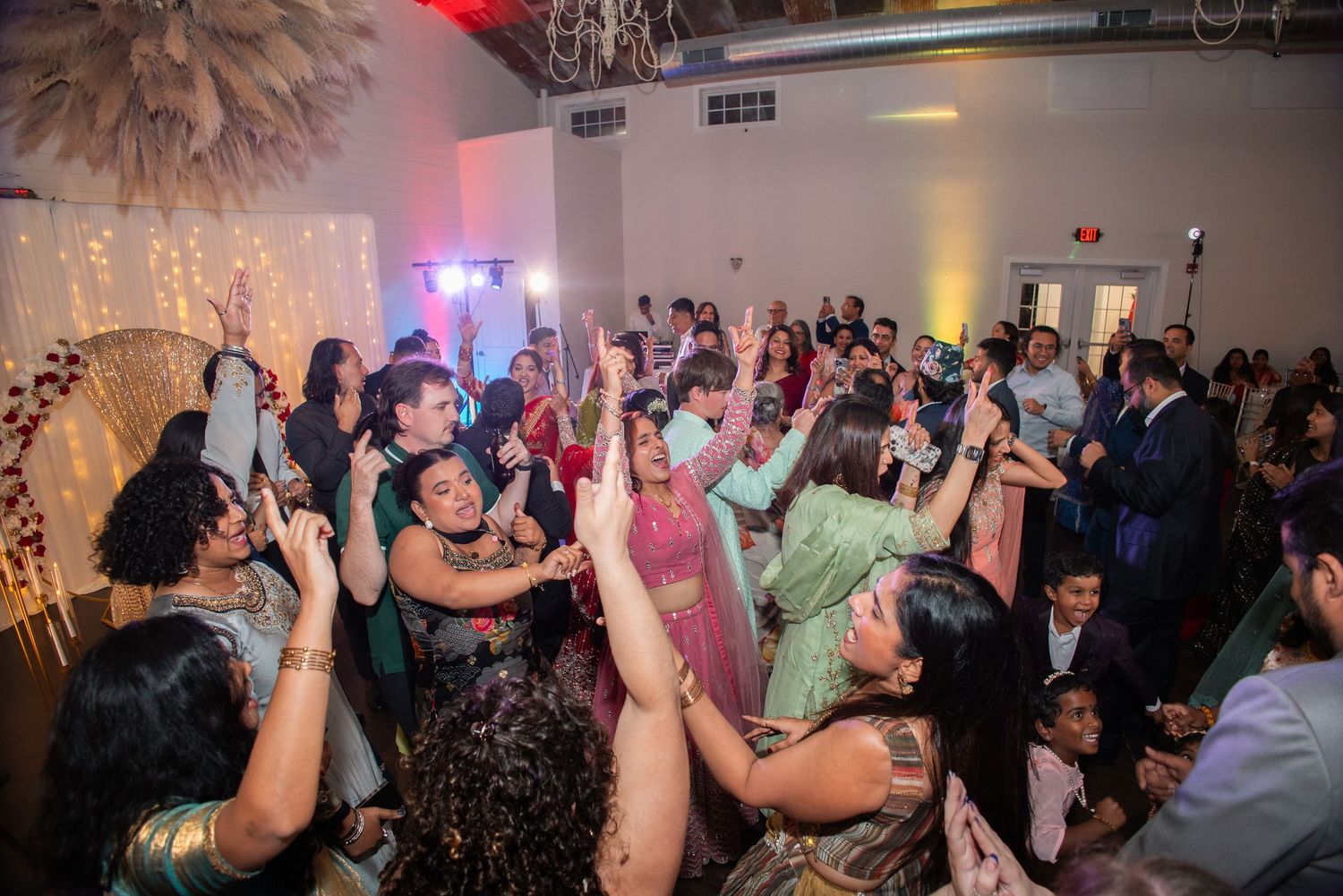 Guests dancing and celebrating at a vibrant Indian wedding reception with colorful attire and festive lighting.