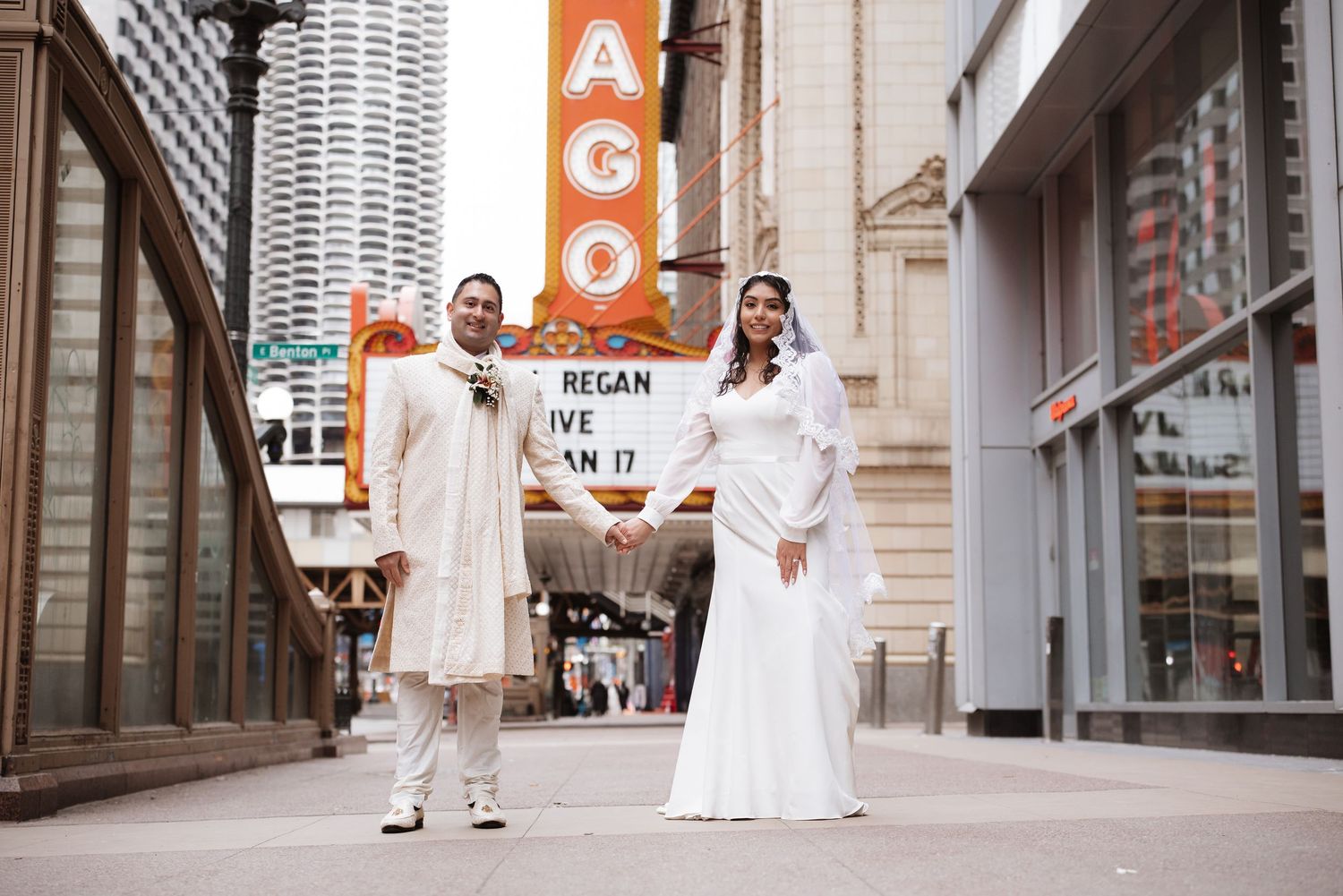 Bride and groom holding hands in front of iconic Chicago Theatre marquee on State Street sidewalk.