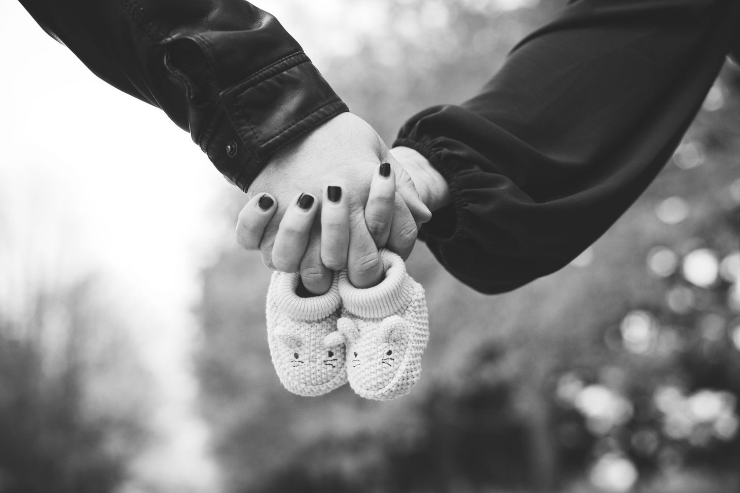 Black and white close-up of couple holding hands and small knit baby booties, pregnancy reveal.