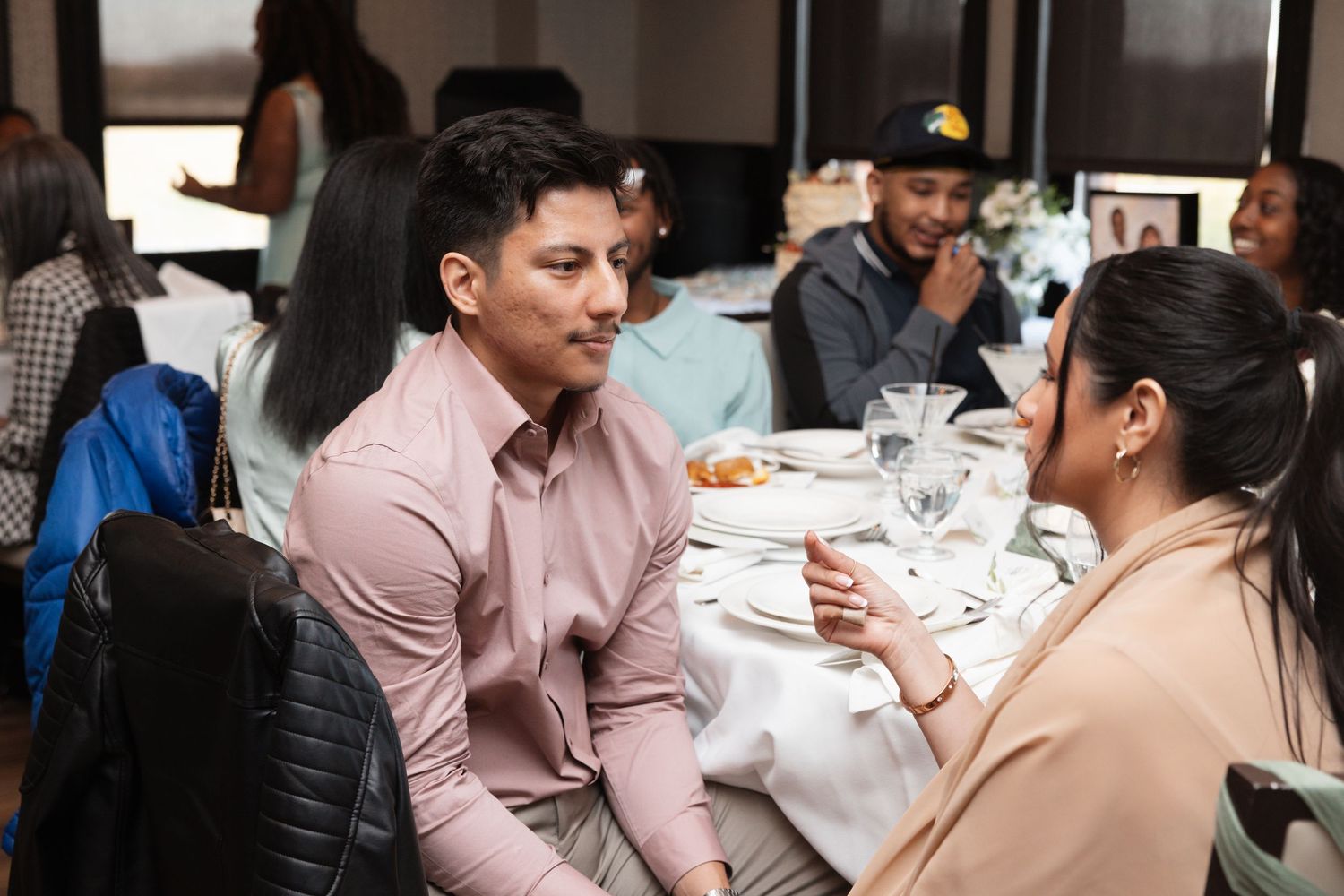 Guests in pink shirts share a conversation at a wedding reception dinner table.