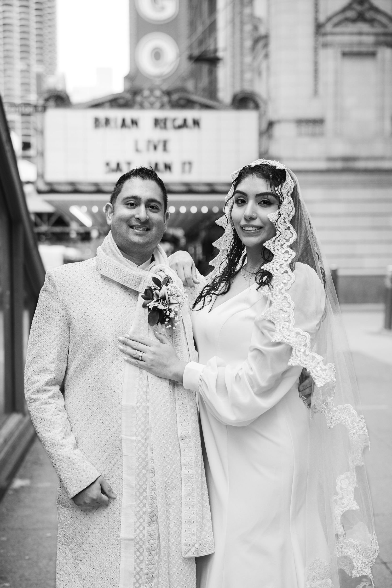 Black and white photo of bride and groom posing outside Chicago Theatre on their wedding day.