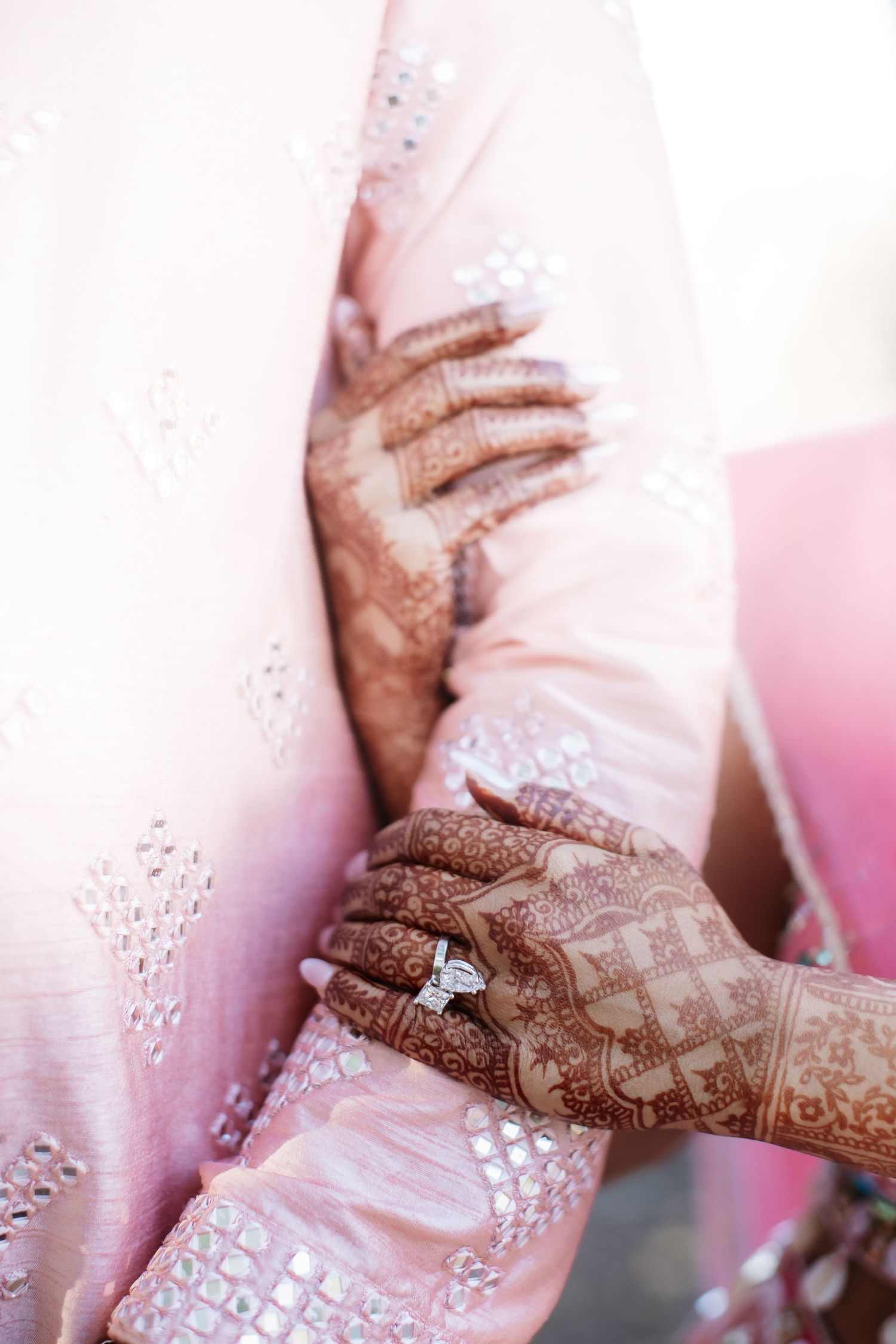 Close-up of brides hands adorned with intricate henna mehndi patterns and a diamond engagement ring.