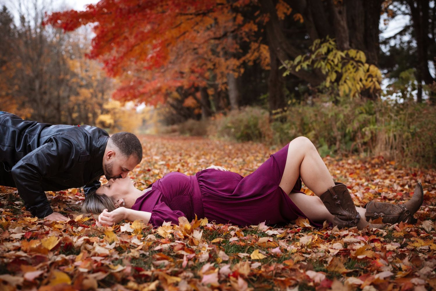 Couple sharing a kiss lying on colorful fall leaves in park.