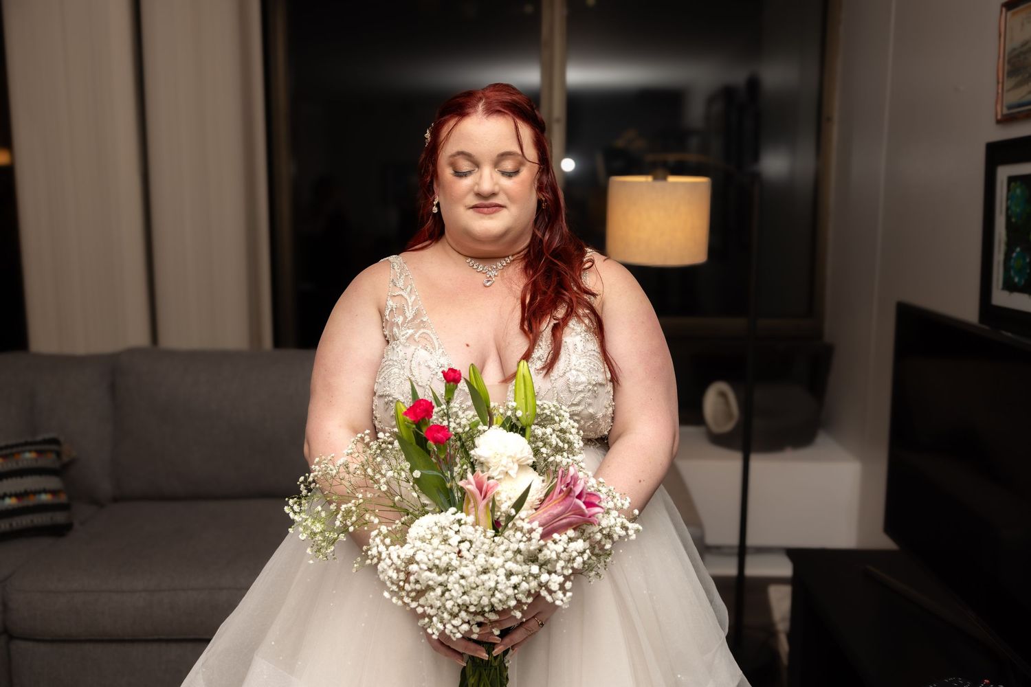 Beautiful plus-size bride with red hair gazes at colorful bouquet of tulips and baby's breath.