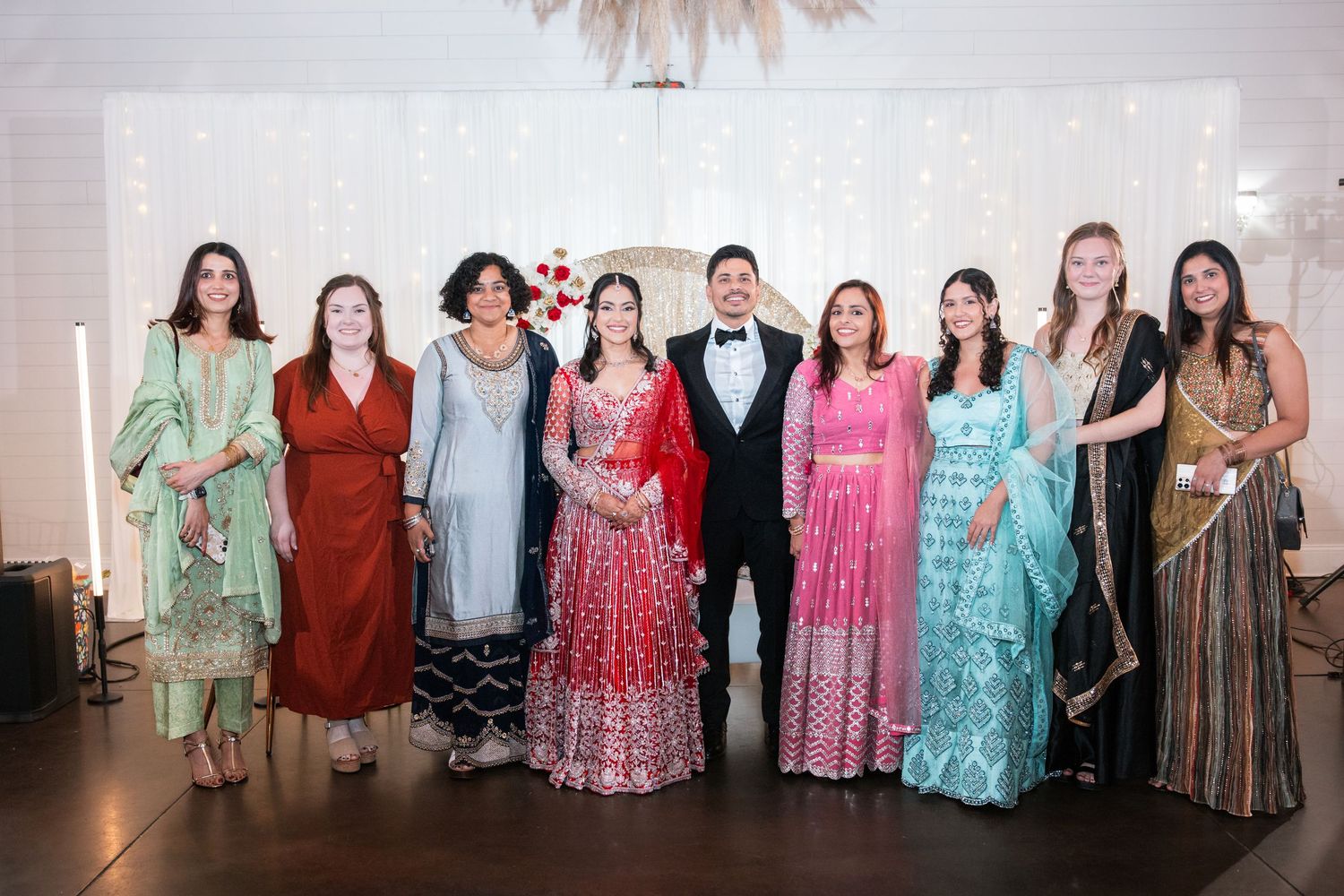 Group of nine people posing together at an Indian wedding reception, women wearing colorful traditional attire.