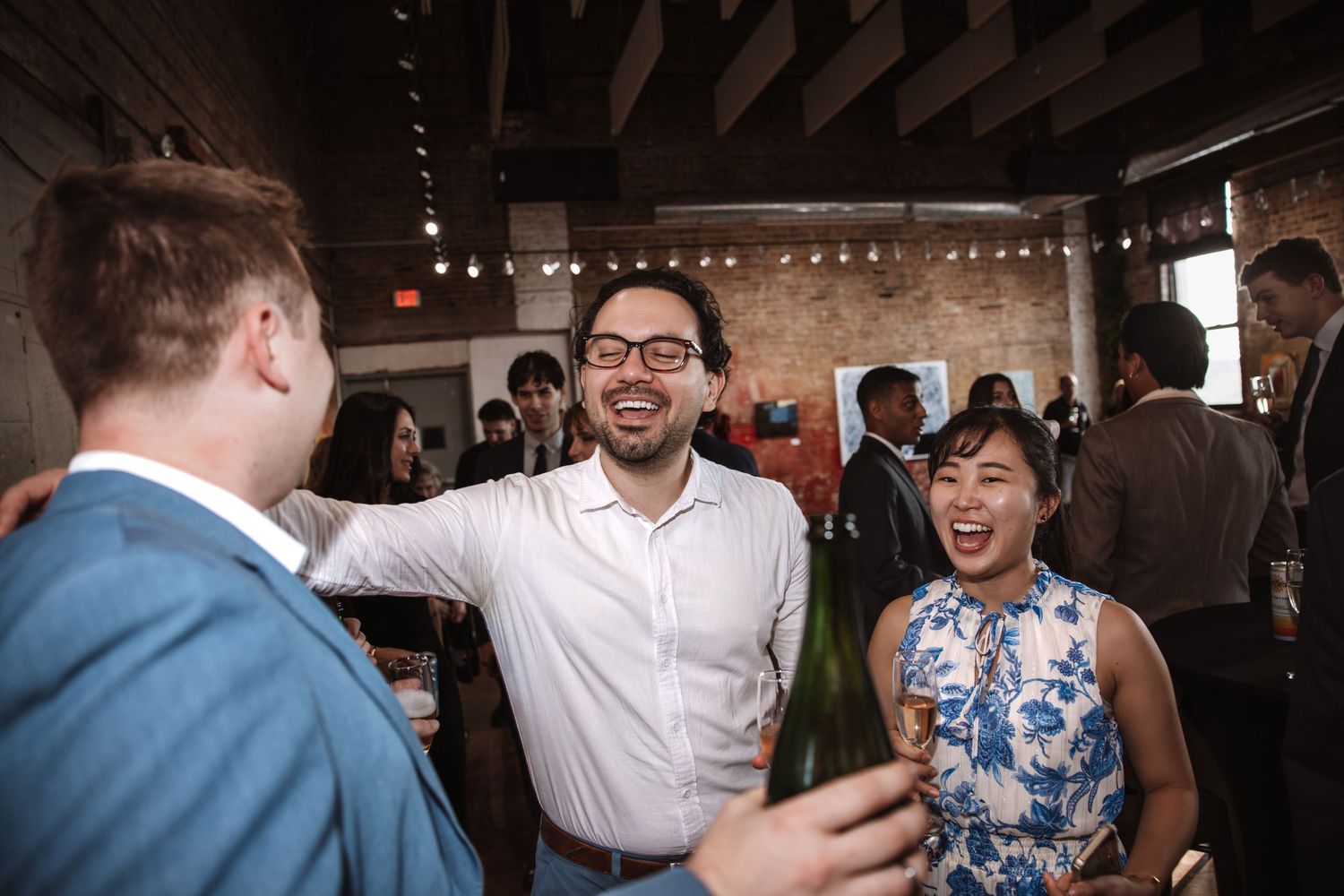 Three guests laugh and share champagne at an elegant indoor cocktail reception.