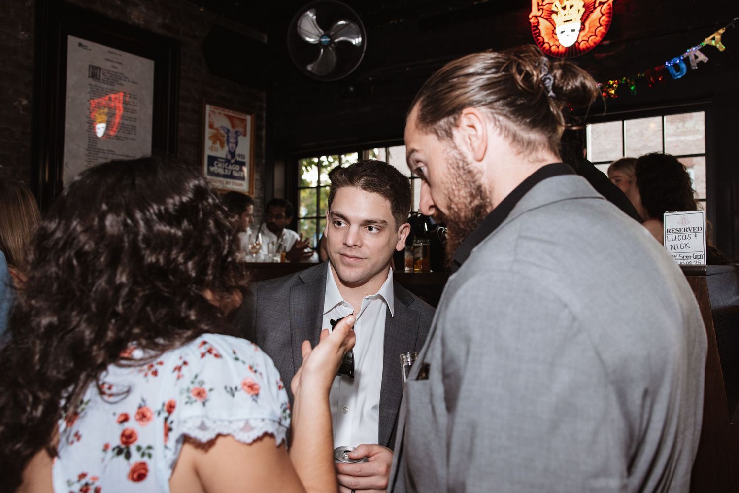 Guests in formal attire engage in conversation at a lively wedding reception bar venue.
