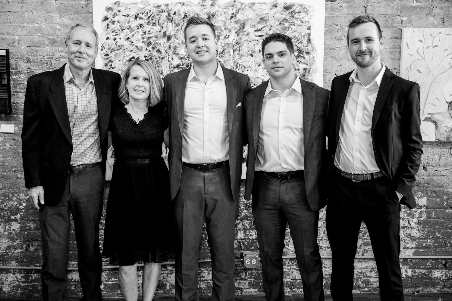Black and white photo of five formally dressed guests posing at an art gallery event.