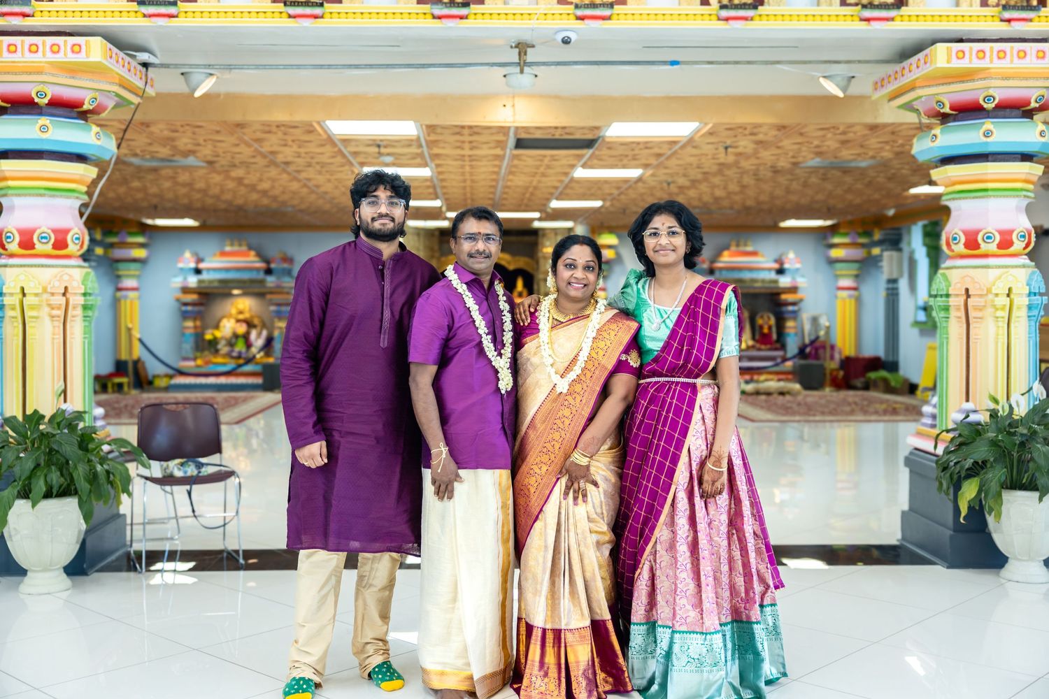 Family of four in traditional Indian attire smiling together inside a beautifully decorated Hindu temple.