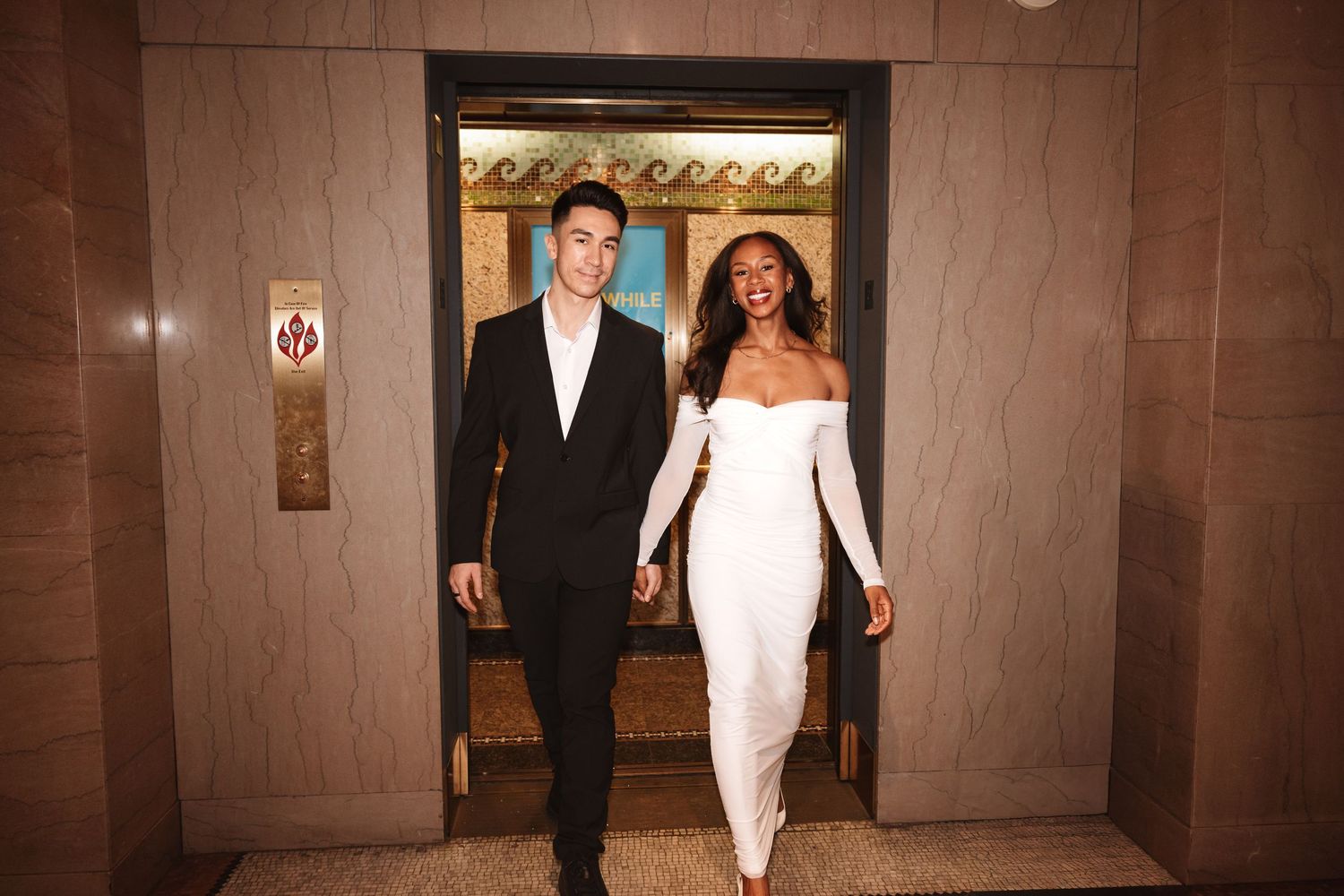 Happy newlywed couple laughing while exiting an elegant elevator, bride in white dress and groom in black suit.Chicago Wedding Photographer