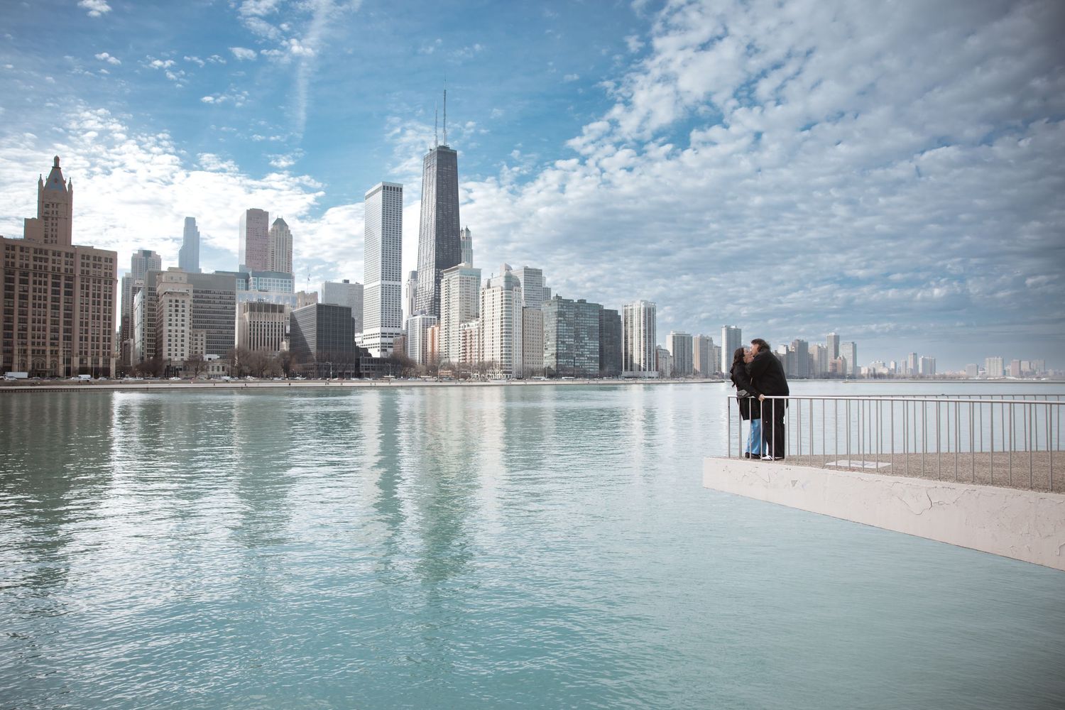 Couple standing on a waterfront pier overlooking the stunning Chicago skyline on a partly cloudy day.