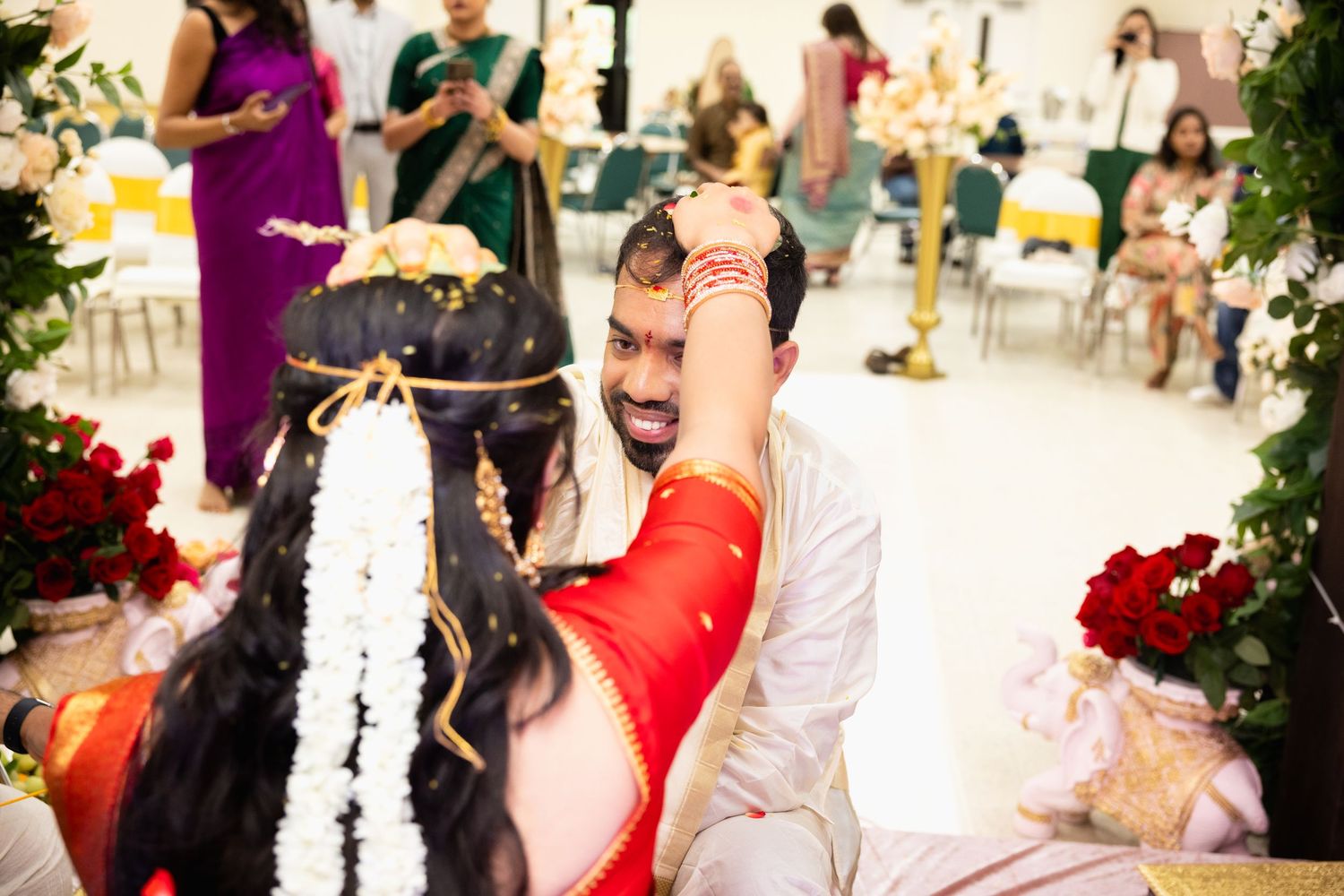 Indian groom applying sindoor to bride during traditional Hindu wedding ceremony with floral decorations.