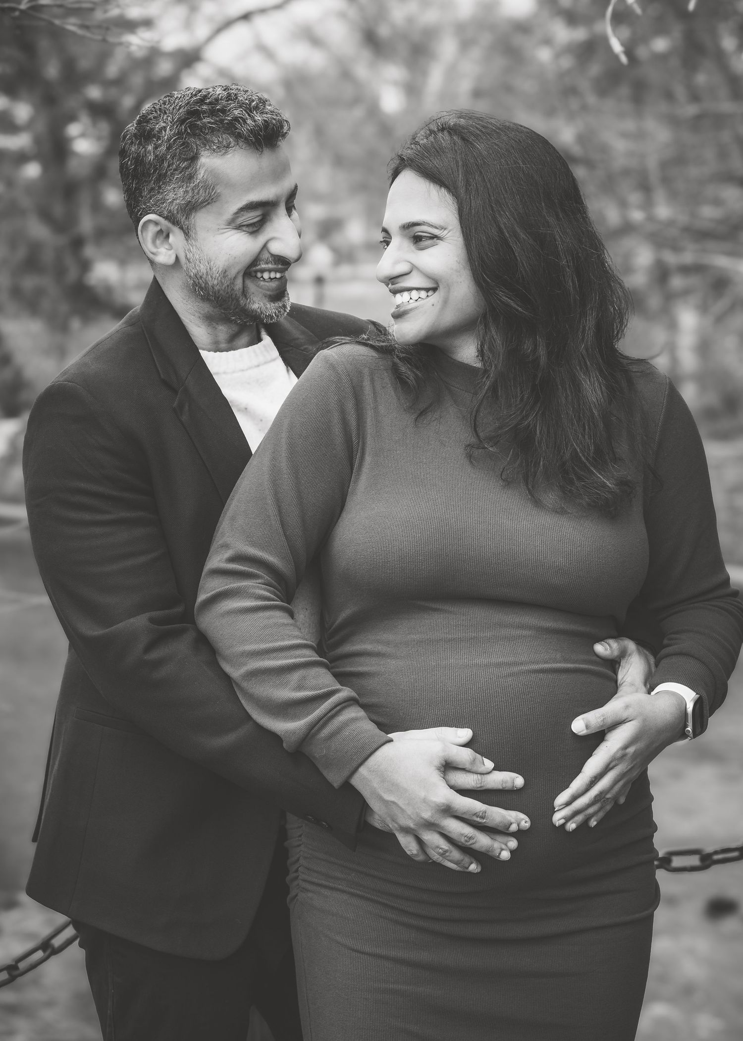Black and white photo of smiling couple during outdoor maternity photoshoot together.
