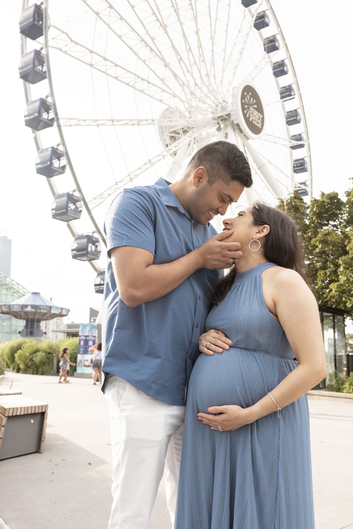 Couple sharing romantic moment near Ferris wheel during maternity shoot.