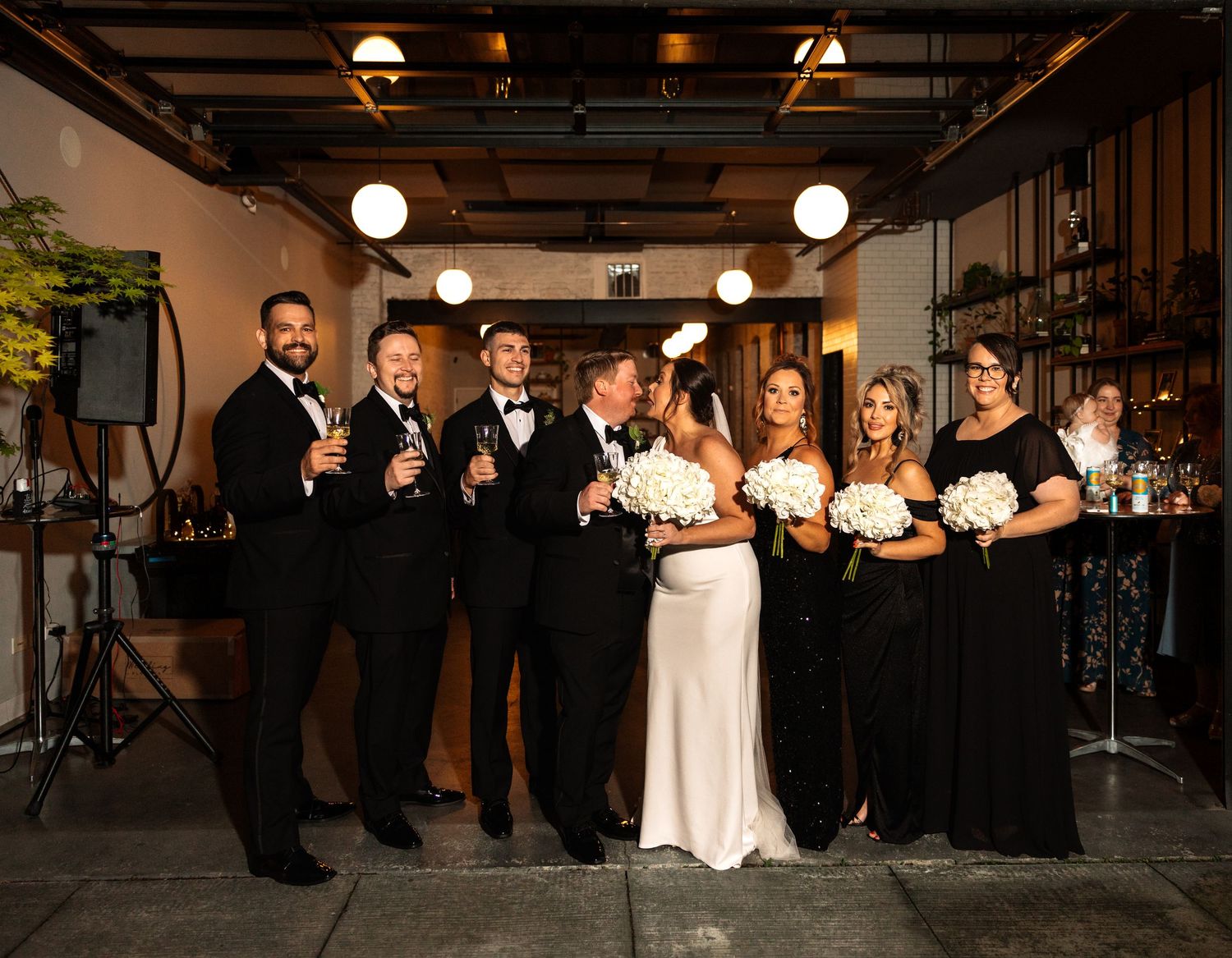 Joyful wedding party laughing together in stylish venue with bride in white gown and guests in black.