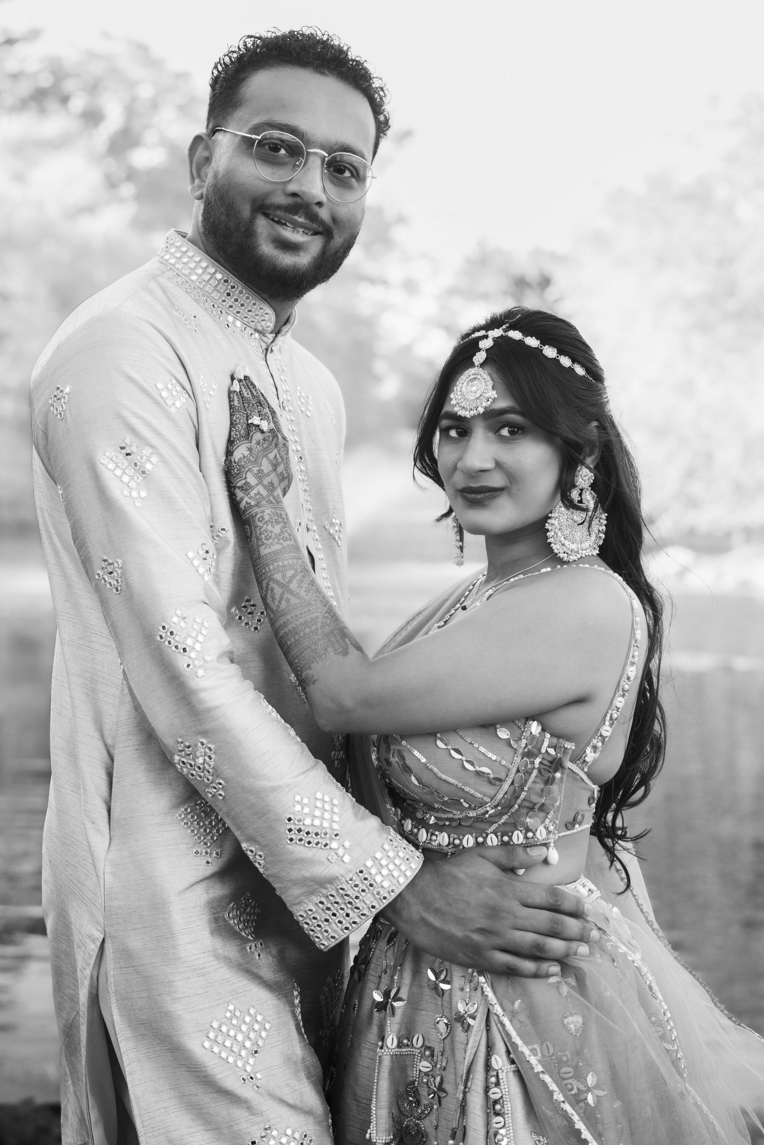 Black and white portrait of Indian couple in traditional wedding attire embracing outdoors.