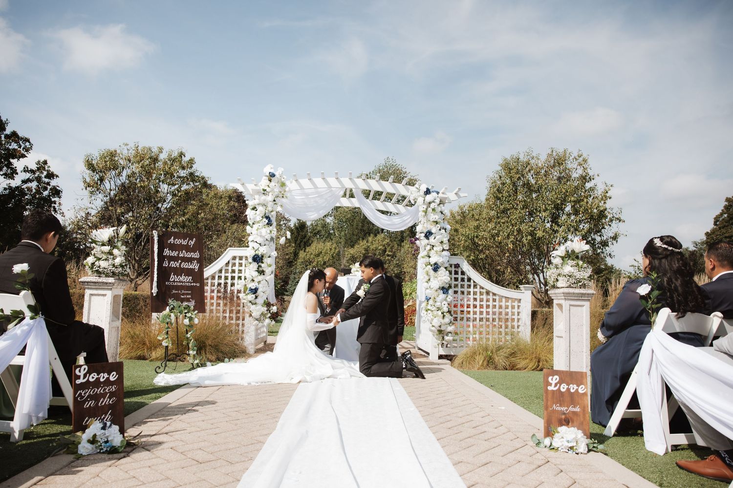 Bride and groom kiss at altar during outdoor wedding ceremony with seated guests watching.