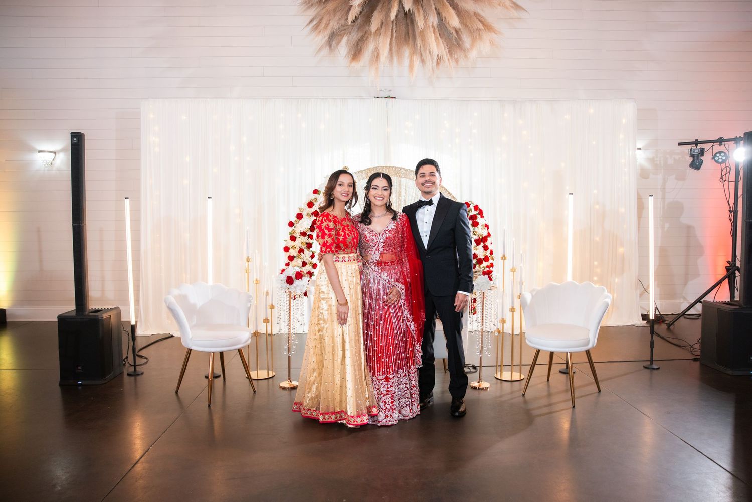Bride in red lehenga poses with two guests at elegant Indian wedding reception venue.