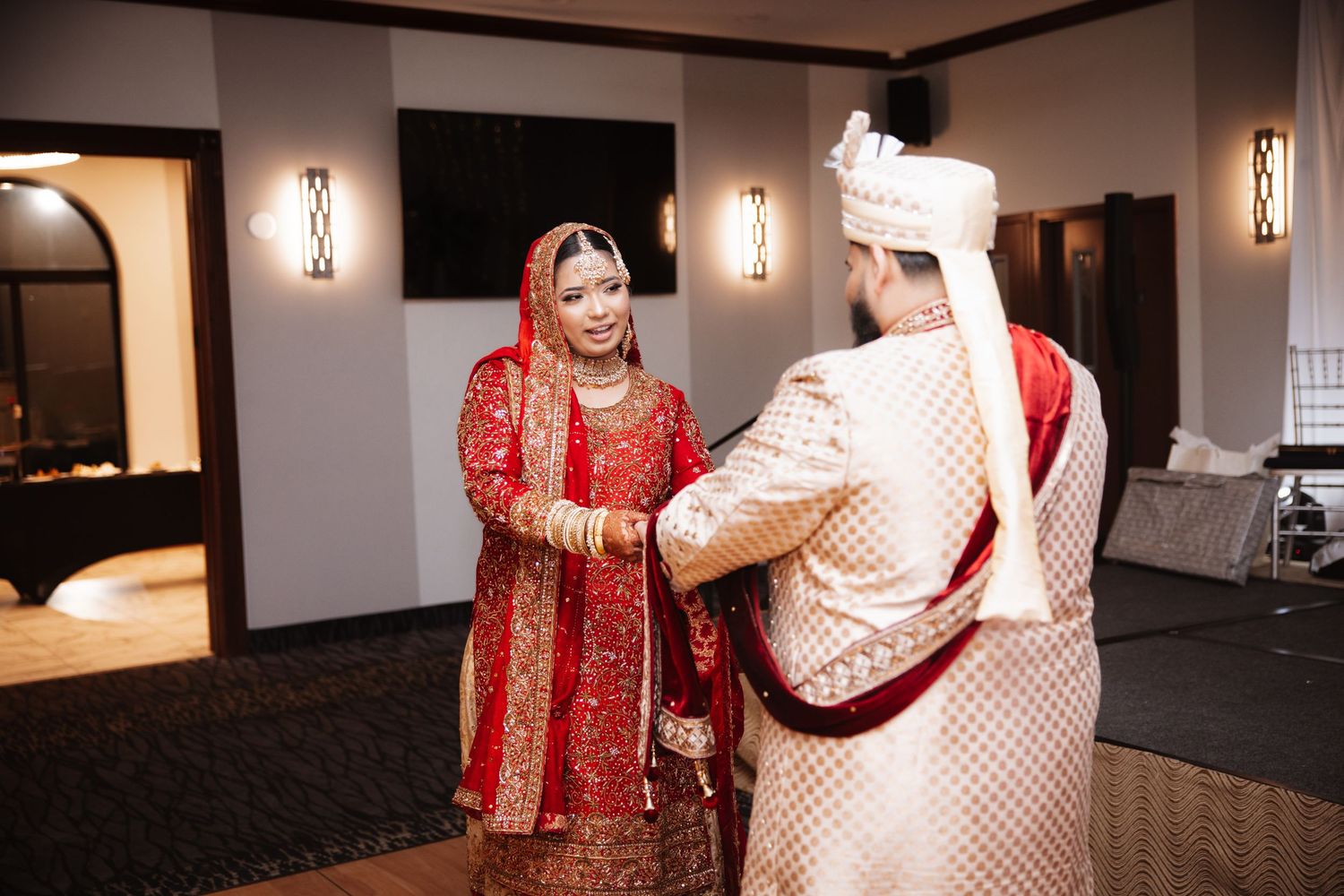South Asian bride and groom in traditional wedding attire sharing an intimate moment indoors.