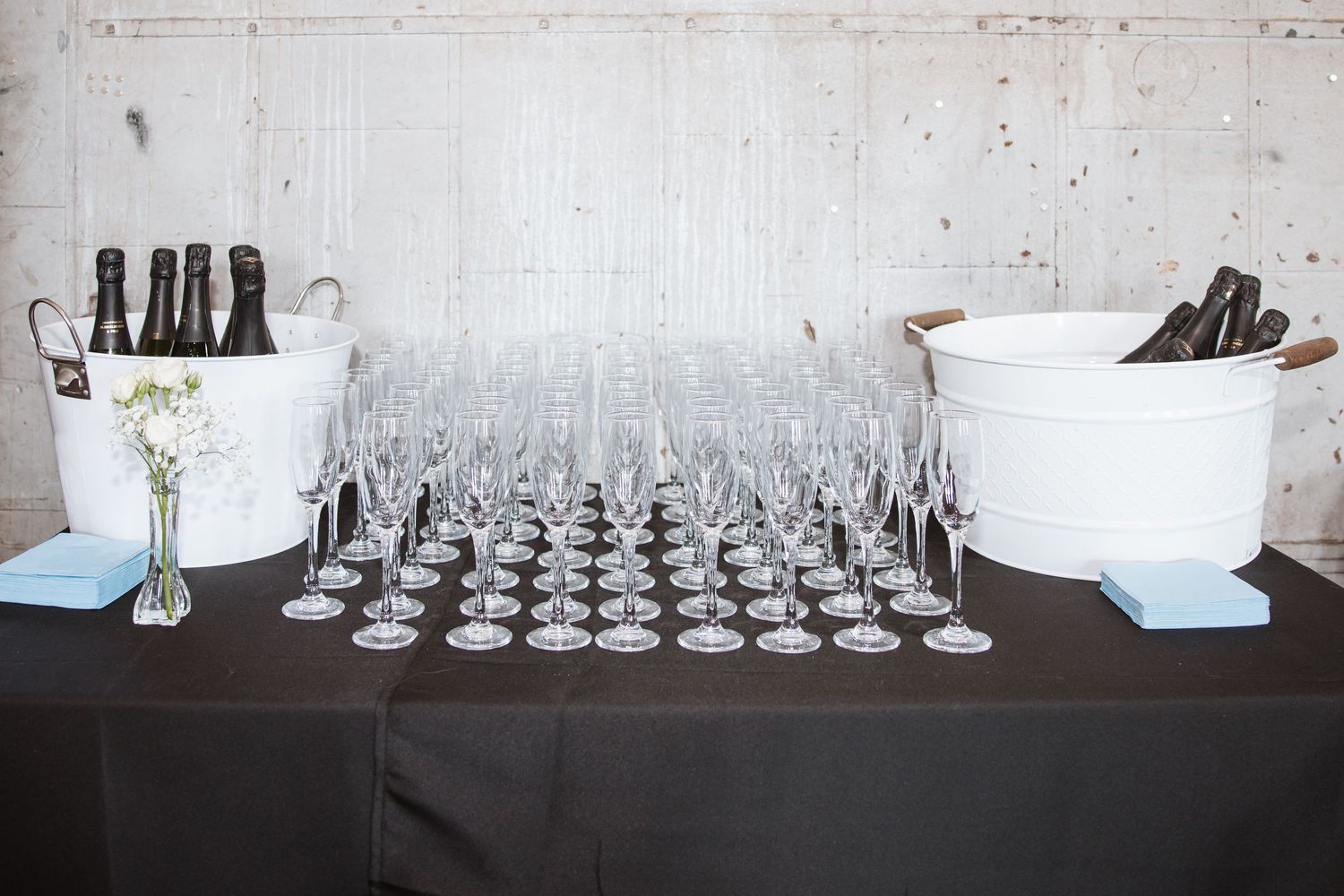 Elegant champagne glasses arranged on a black tablecloth with wine bottles chilling in ice buckets at a wedding reception.