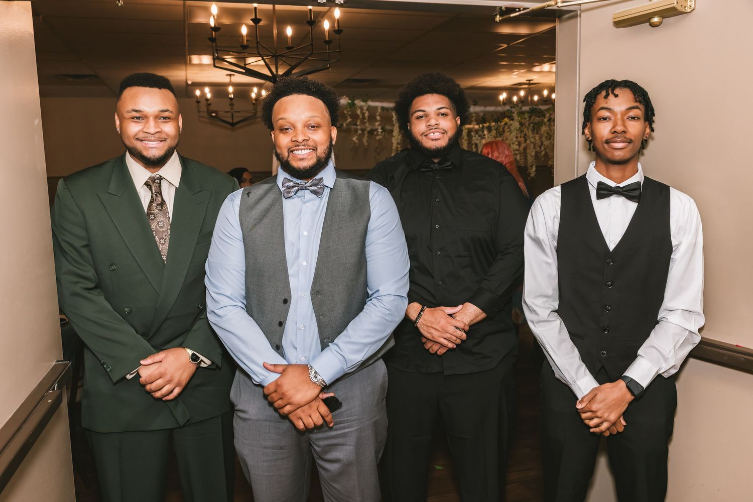 Four young men in formal attire pose together smiling at an elegant wedding reception event.
