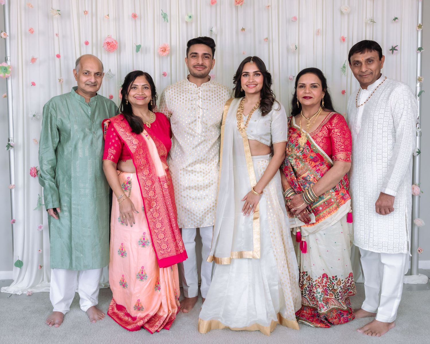 Six people in traditional Indian clothing pose together at a wedding, featuring colorful sarees and kurta pajamas.