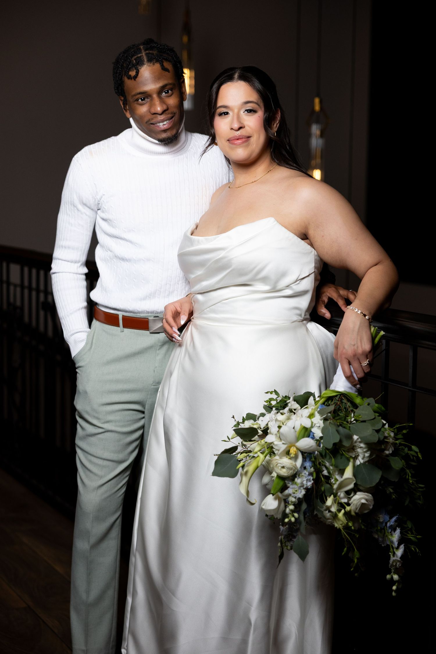 Bride and groom posing together, bride in white strapless gown holding white floral bouquet.