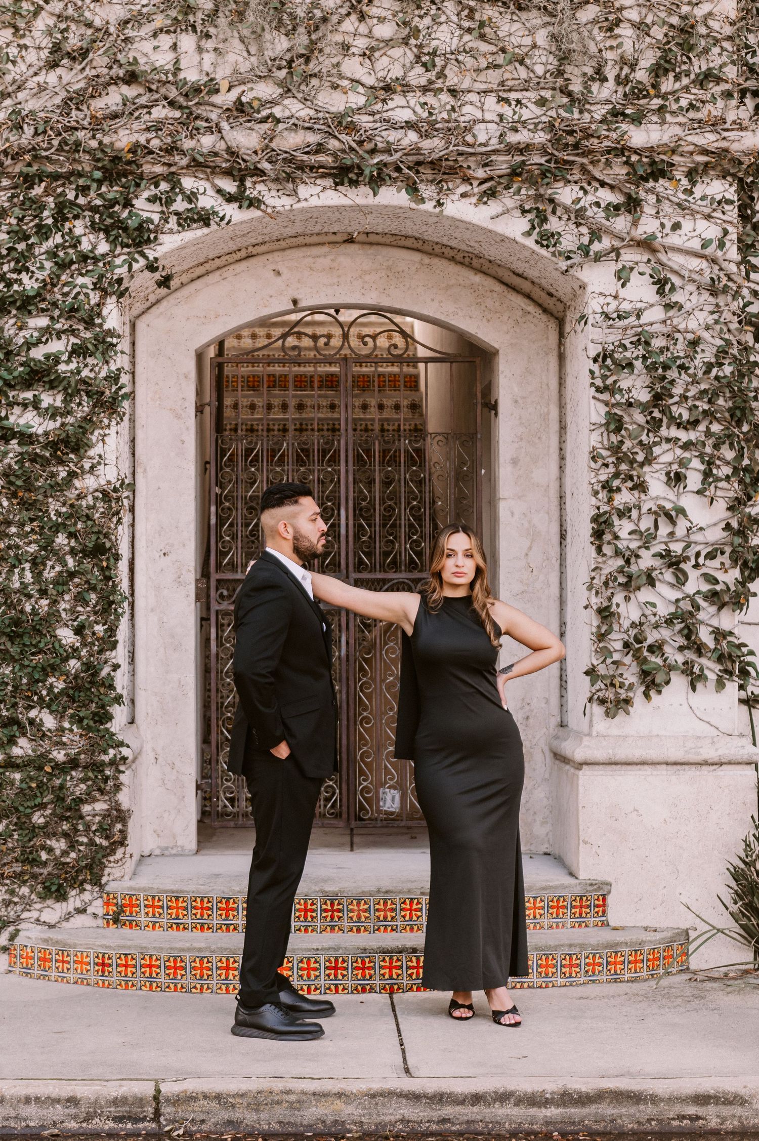 Stylish couple poses against ornate architectural backdrop during photo session.