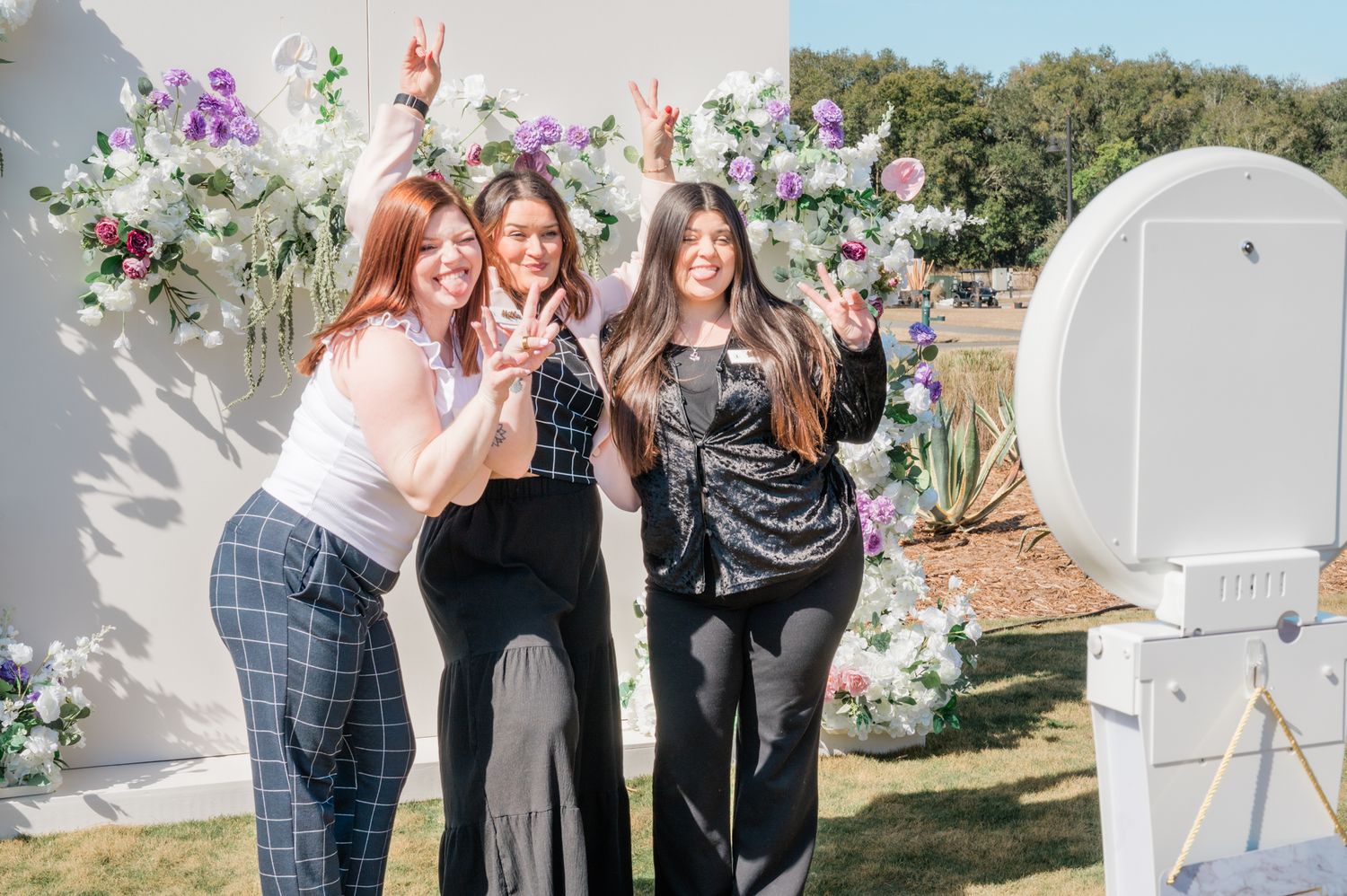 A group of people celebrate together in an outdoor garden setting with floral decorations and white furniture.