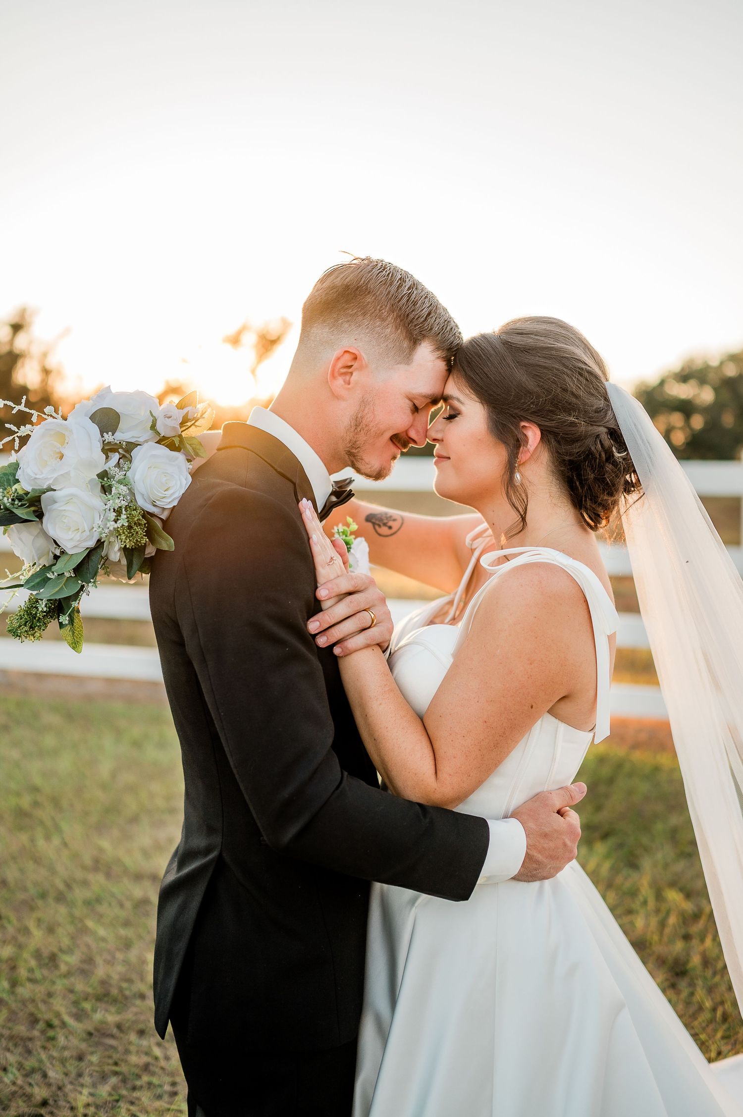A romantic wedding couple embraces during golden hour sunset in a beautiful outdoor setting.