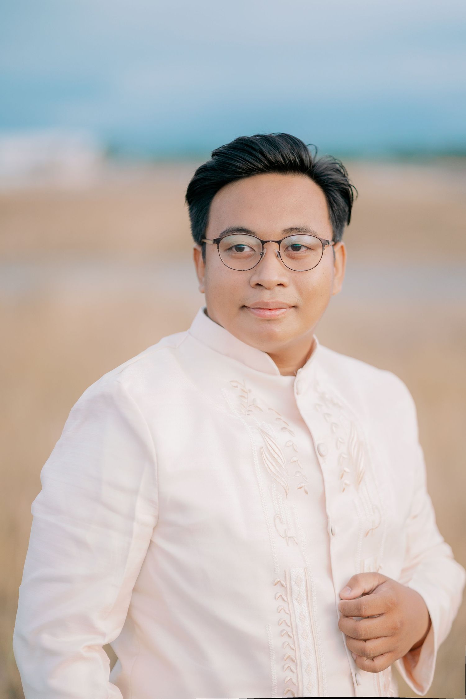 Young man in traditional Filipino Barong Tagalog poses outdoors on a beach with a warm, natural background.