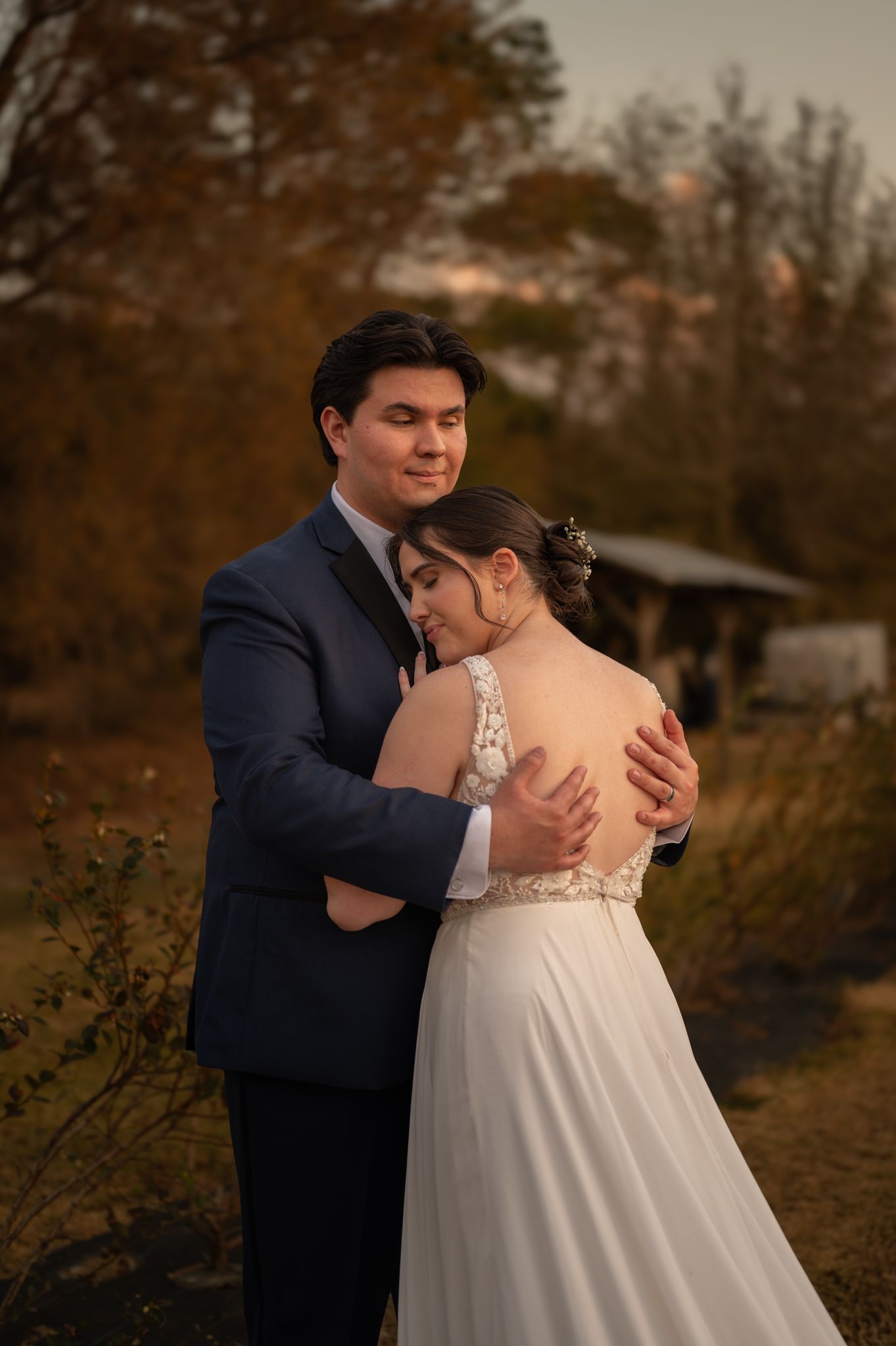 A tender embrace between newlyweds in an autumn outdoor setting with warm lighting and natural scenery.