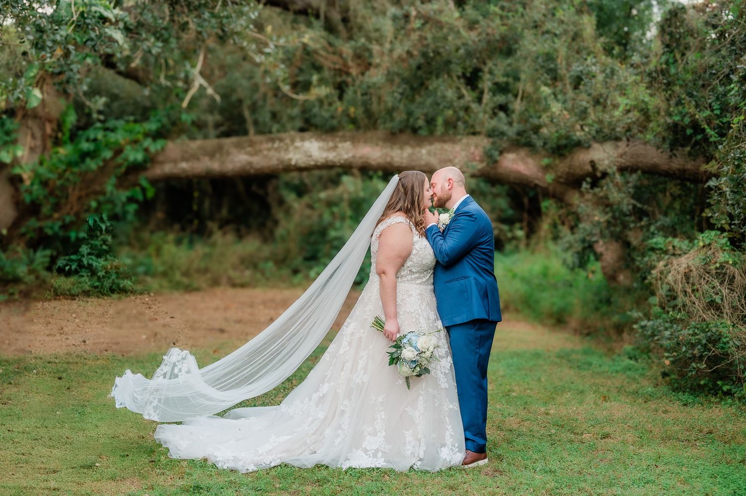 A romantic wedding couple shares tender moments in a lush garden setting with flowing white veil and blue suit.
