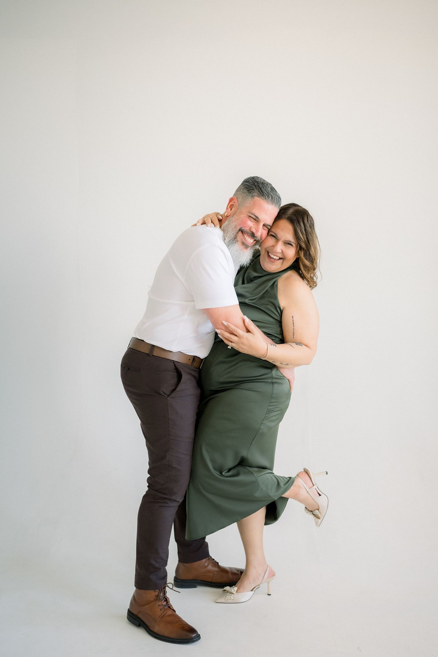 A couple in casual attire shares a playful moment against a white backdrop in a series of candid poses.
