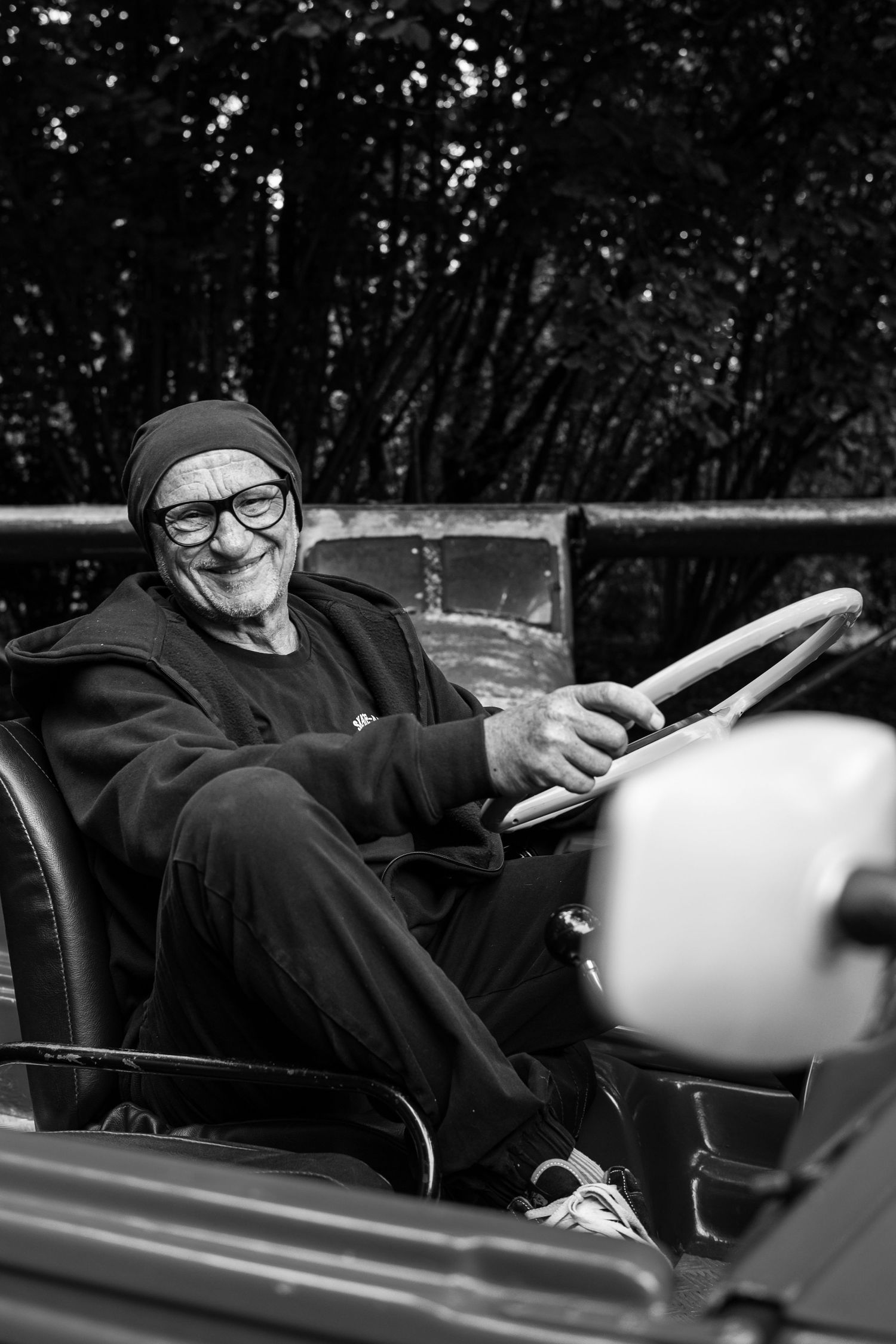 A black and white photo sequence shows someone in dark clothing and glasses sitting in a convertible car.