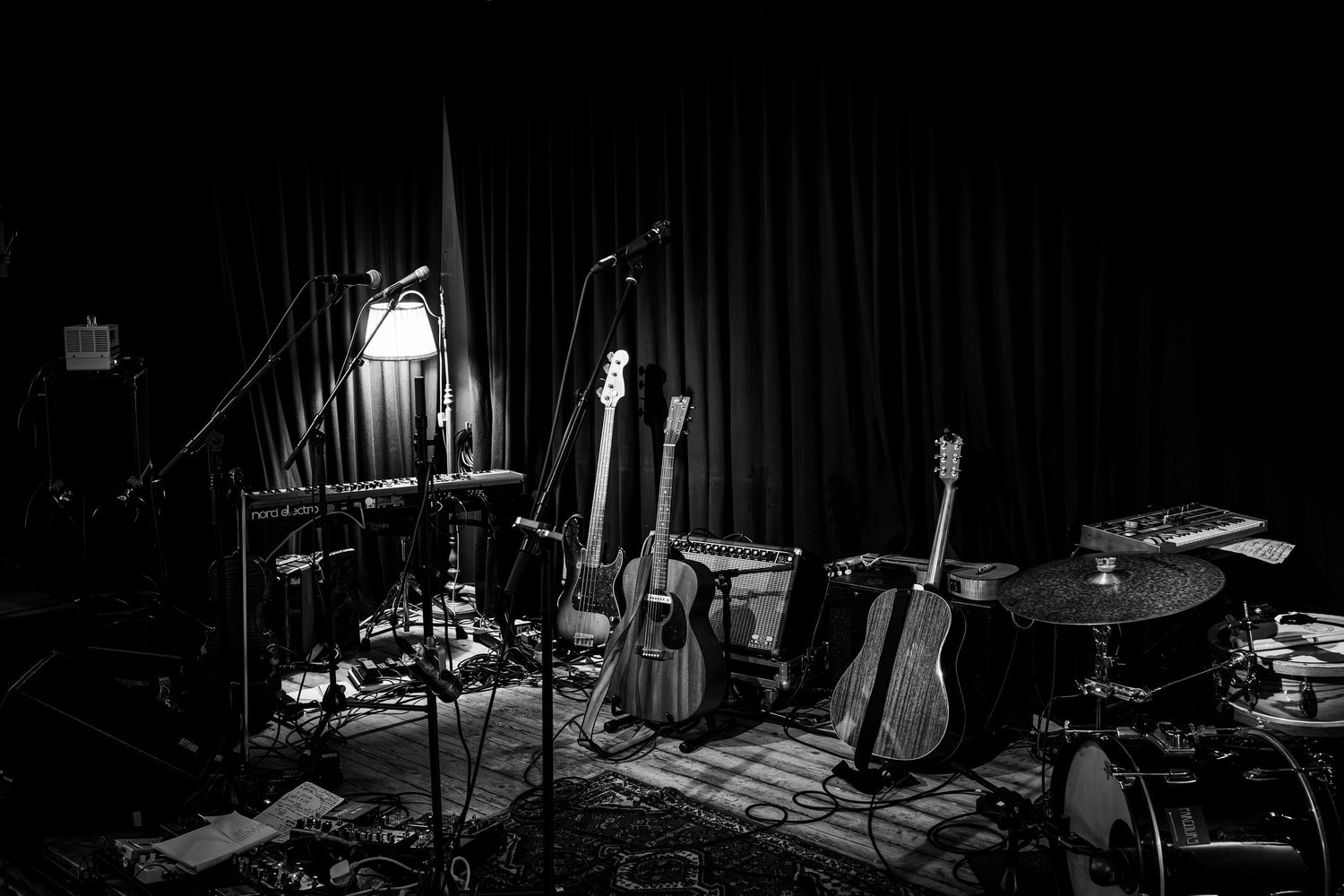 Black and white photo of a dark stage with dramatic lighting and musical instruments silhouetted in the shadows.