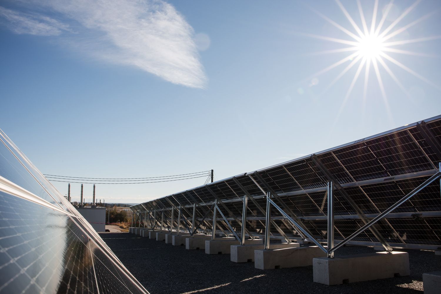 Solar panels installed on a commercial rooftop with bright sunburst and blue sky in the background.