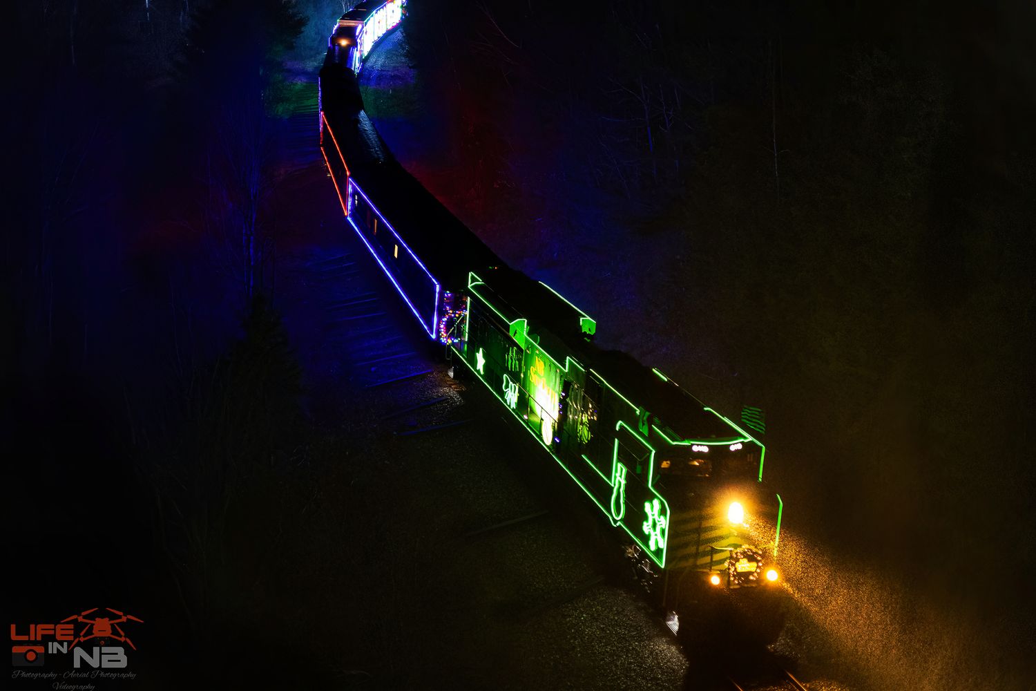 CPKC Holiday Train train moving through darkness with colorful lights creating a dramatic nighttime scene, leaving Saint John, NB.