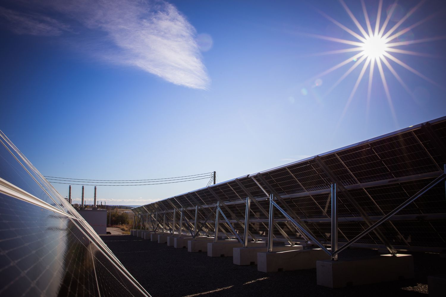 Solar panels silhouetted against bright blue sky with dramatic sunburst effect, in Saint John, NB.