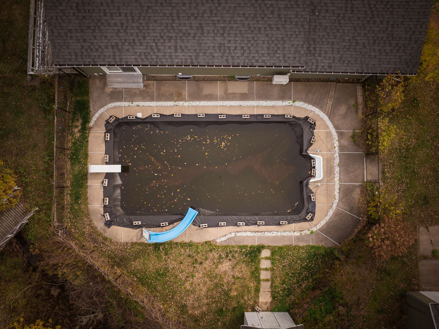 Aerial view of an empty swimming pool with fallen autumn leaves and a blue water slide in a backyard near Saint John.