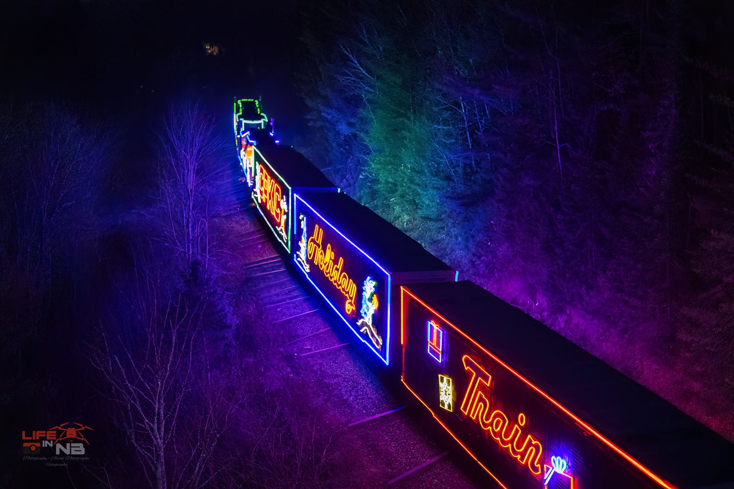 CPKC Holiday Train decorated with bright neon lights glowing against a dark purple background, leaving Saint John, NB
