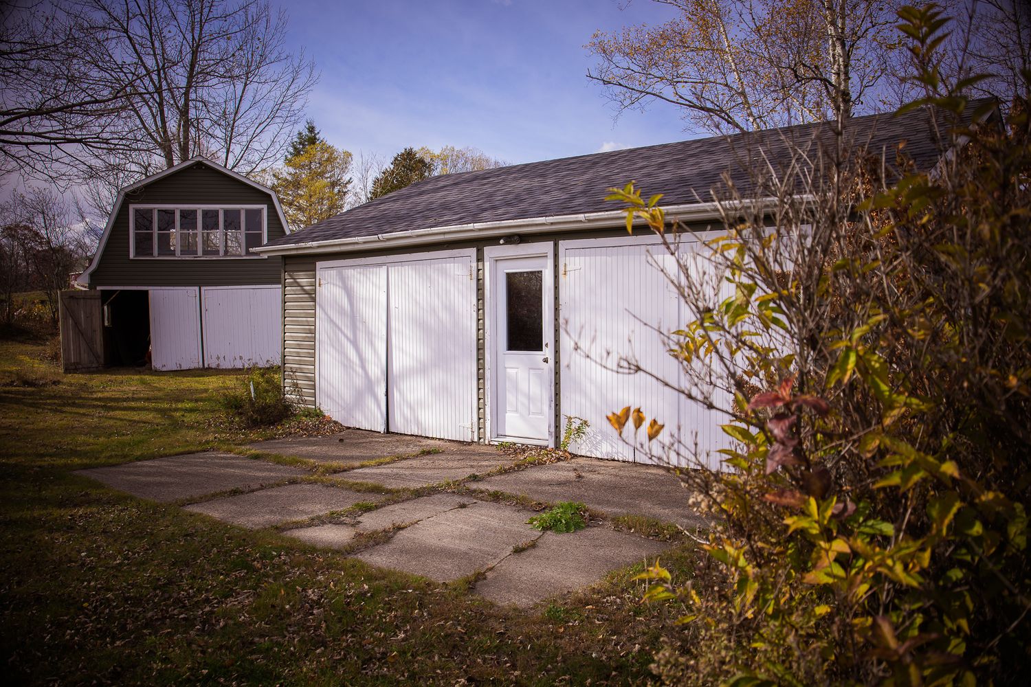 White garage with concrete driveway and autumn foliage in the background near Saint John.