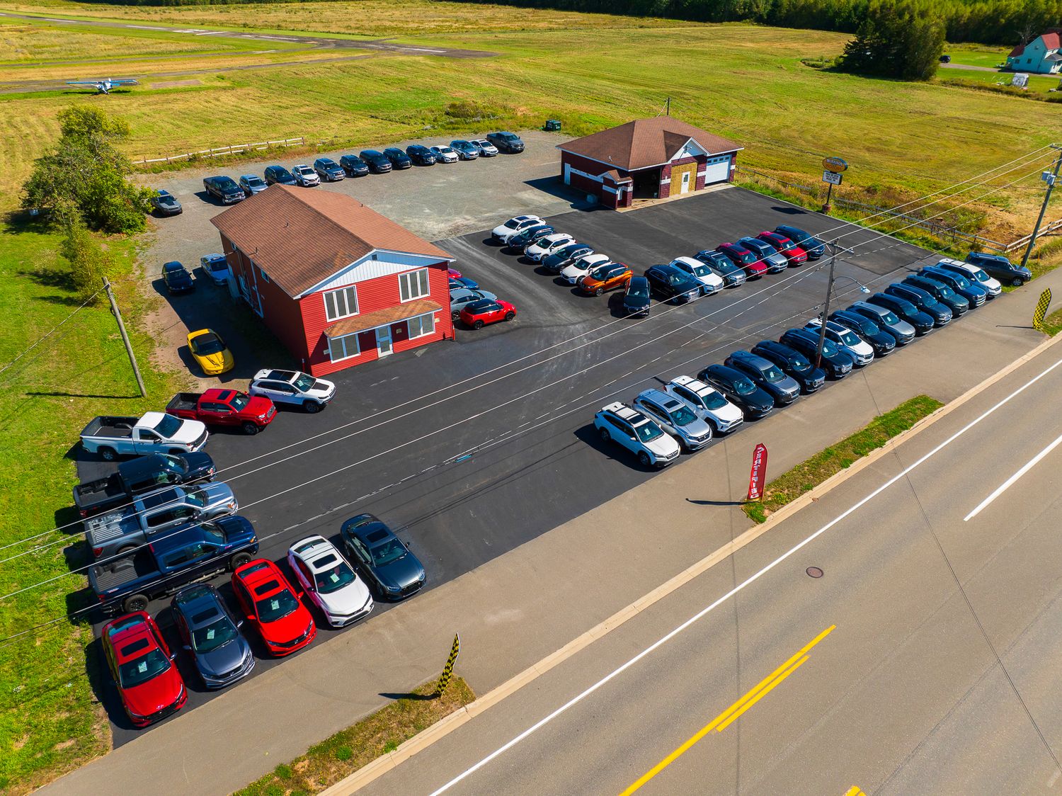 Aerial view of a red commercial car dealership building with multiple cars parked in organized lots, in Moncton.