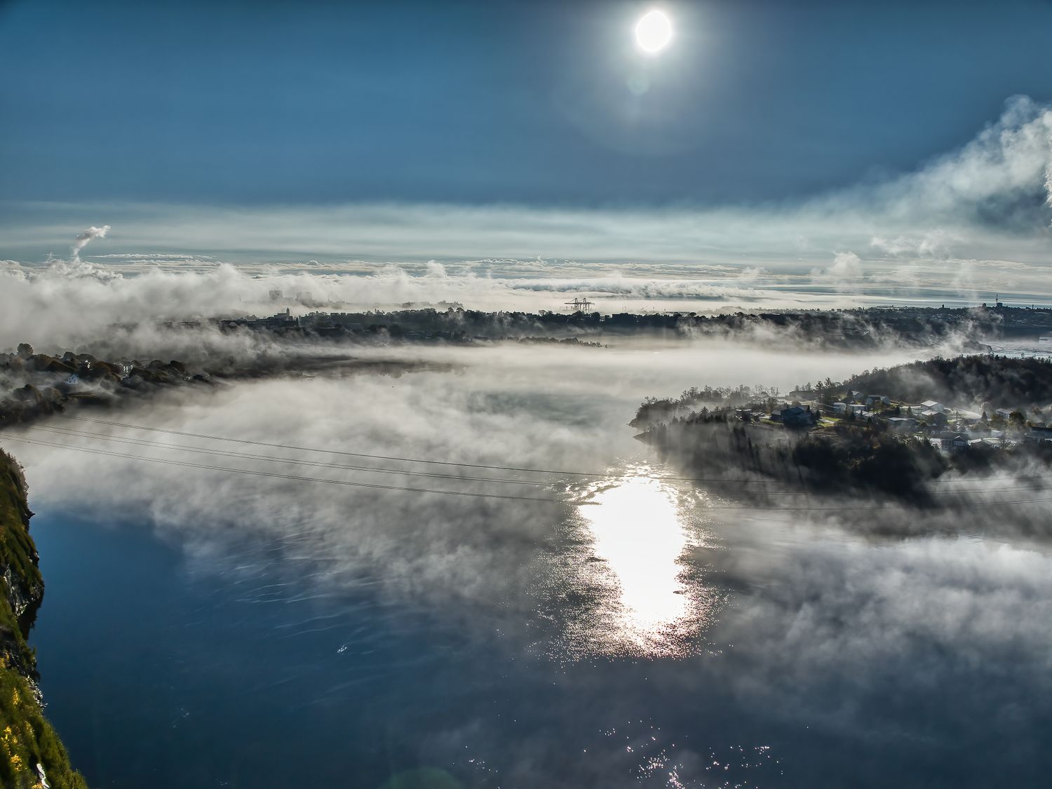 Morning fog rolls across a serene river with sunlight reflecting off the water's surface and misty clouds hovering above Saint John river.