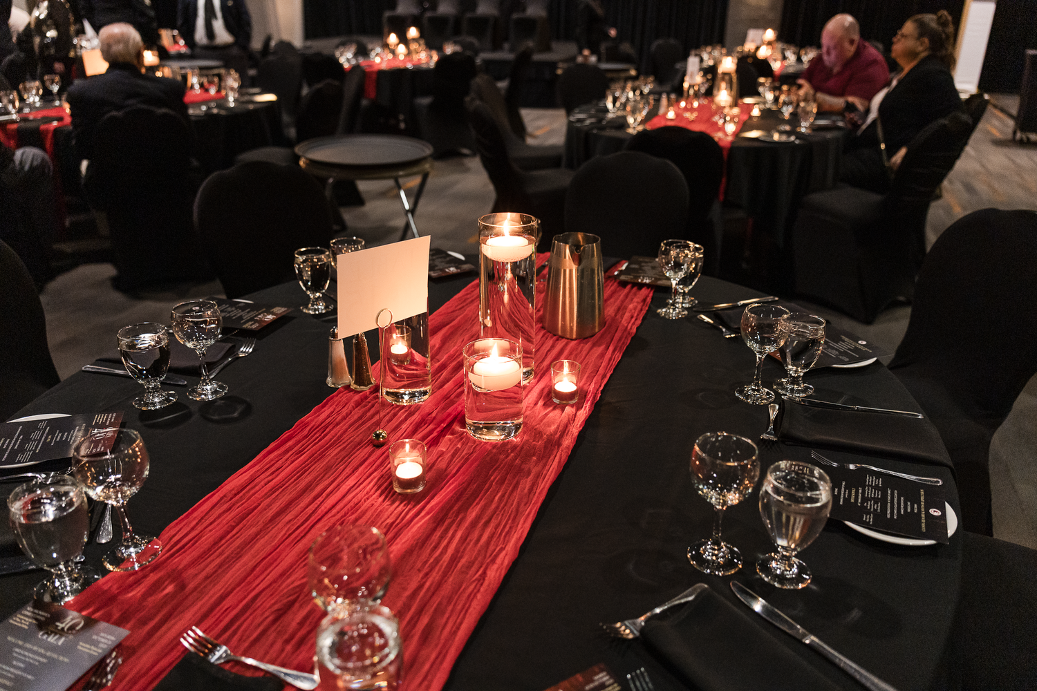 Elegant wedding reception tables with black tablecloths and red table runners lit by candlelight in Saint John, NB.