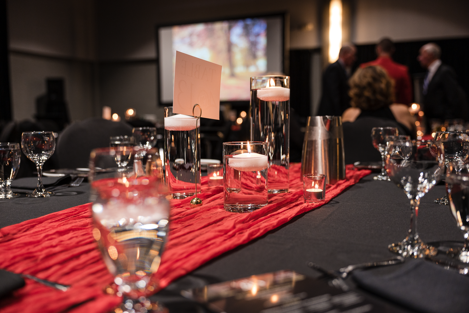 An elegant table setting with black tablecloth, red runner, and floating candle centerpieces in glass cylinders.